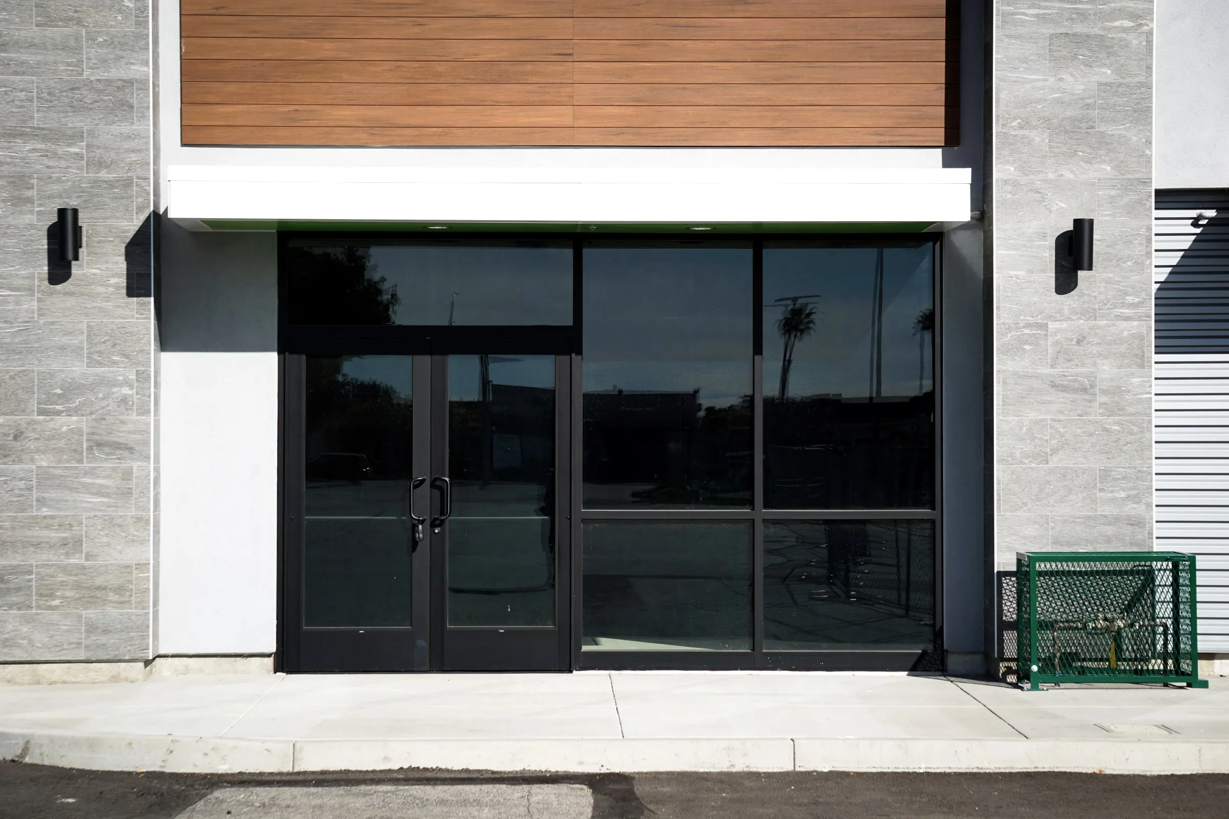 Modern storefront with black-framed glass doors, stone cladding and a bench outside