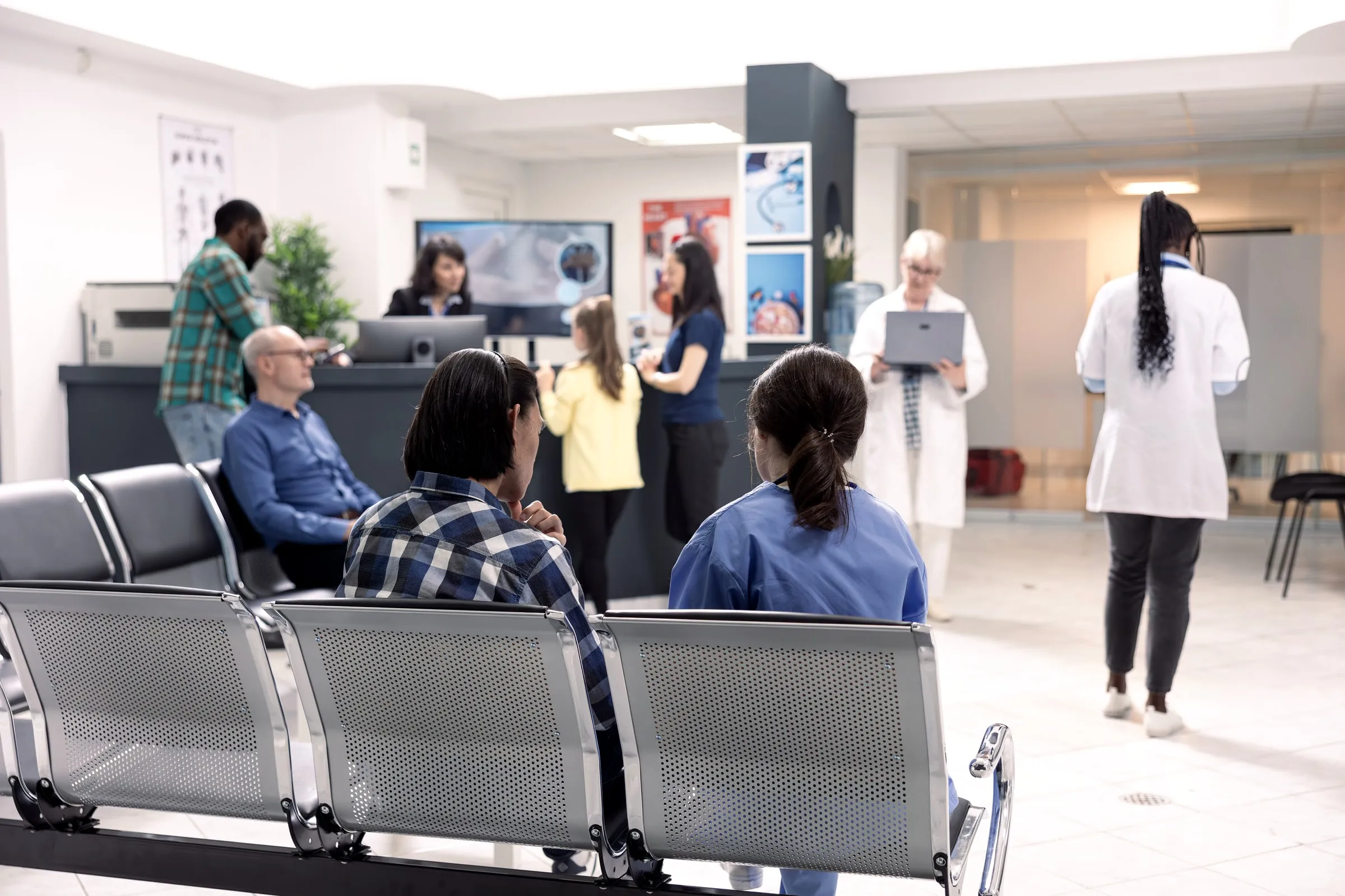 Clinic waiting room with rows of chairs, patients waiting and staff at a reception desk