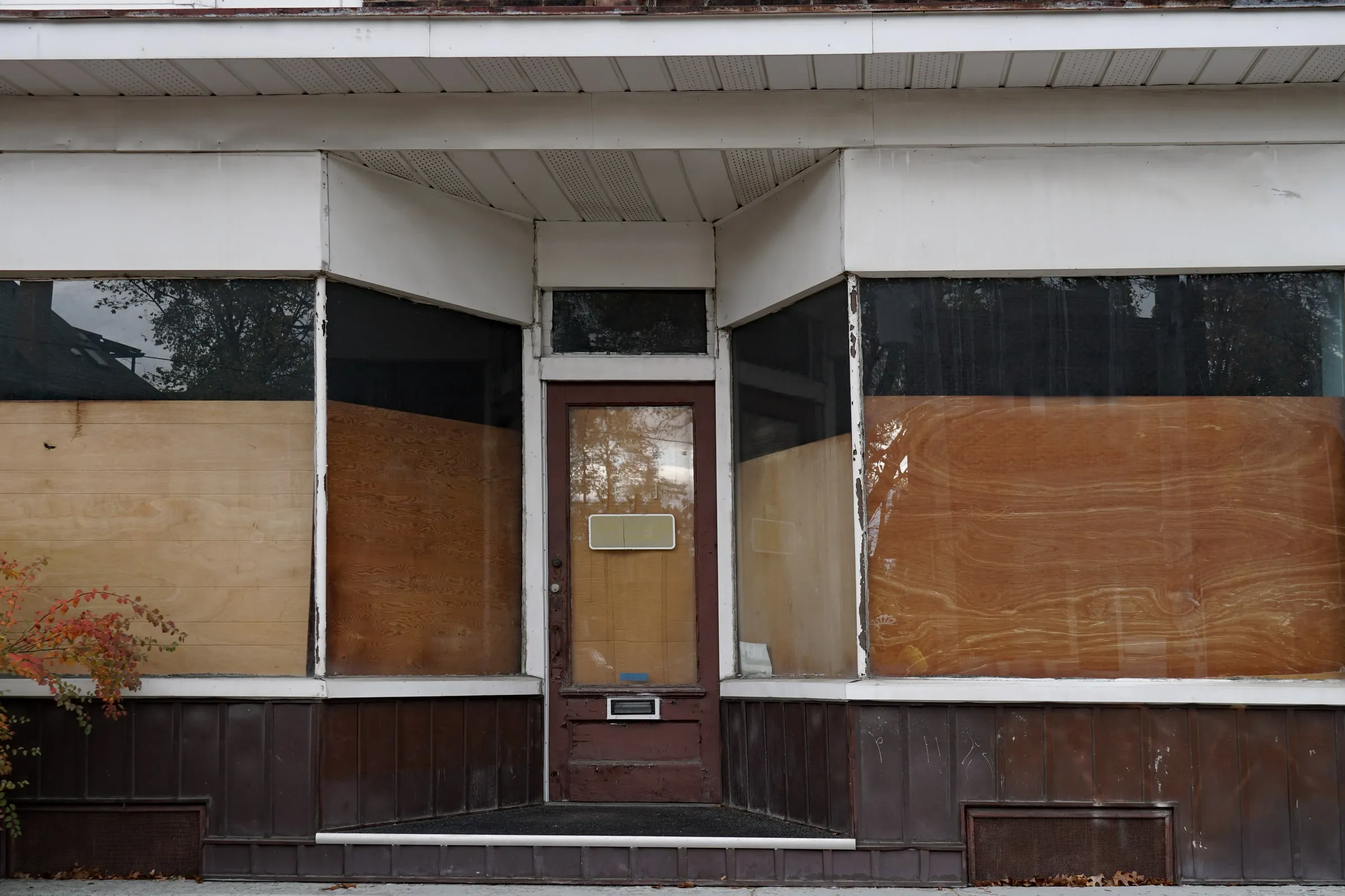 Boarded-up storefront with plywood over the windows and door, peeling paint above