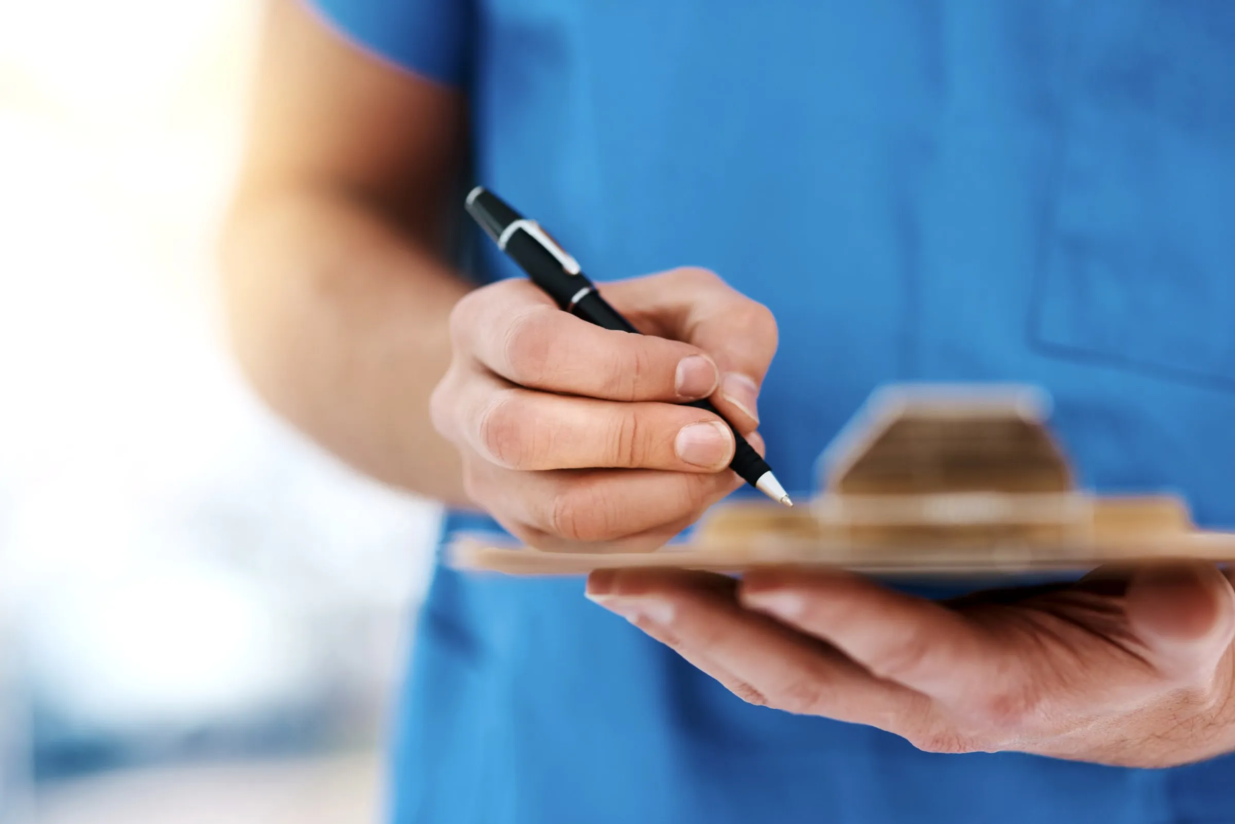 Close-up of a hand in a blue uniform writing with a pen on a small clipboard