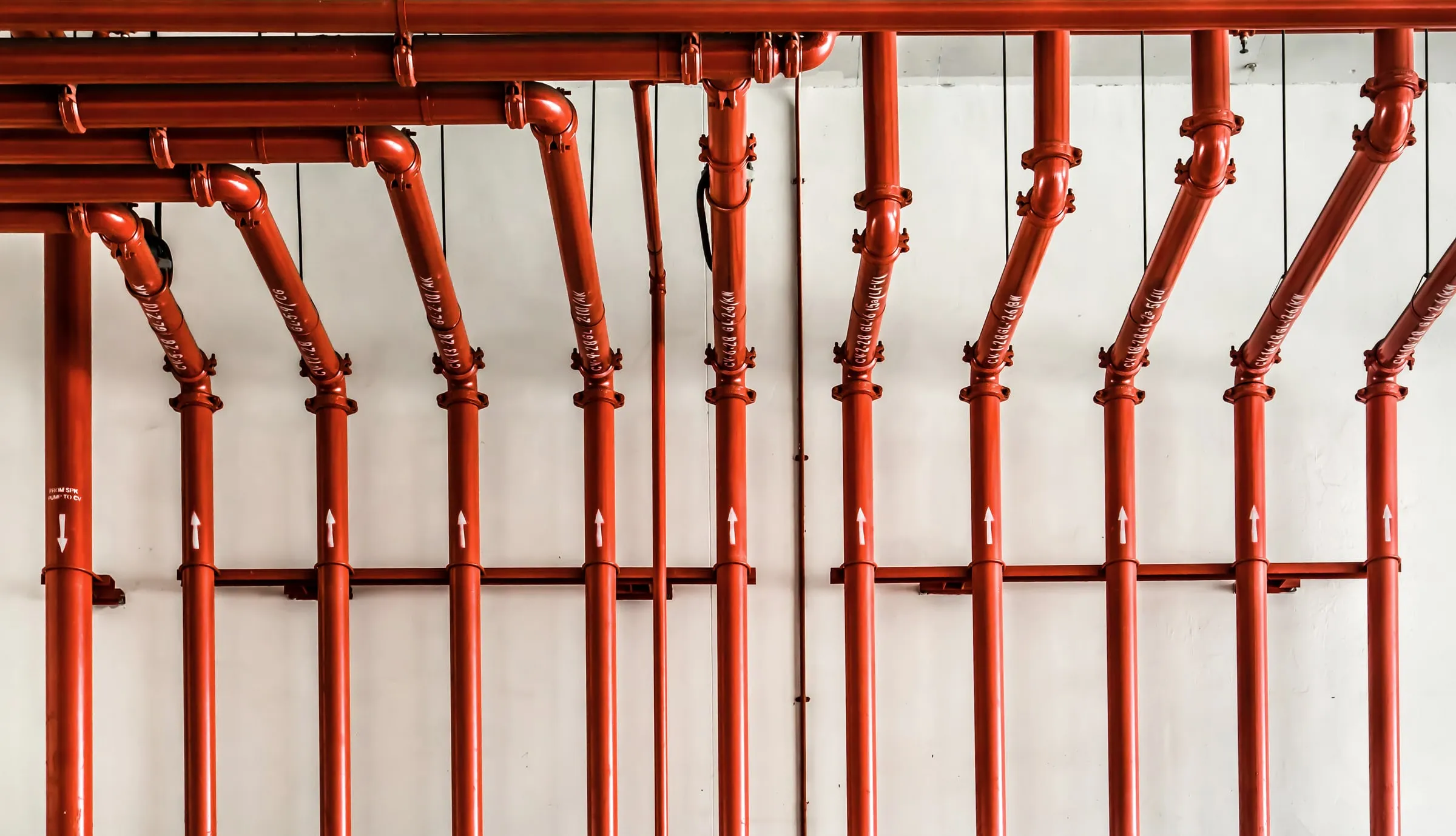 Row of red fire sprinkler riser pipes with gauges mounted along a white wall
