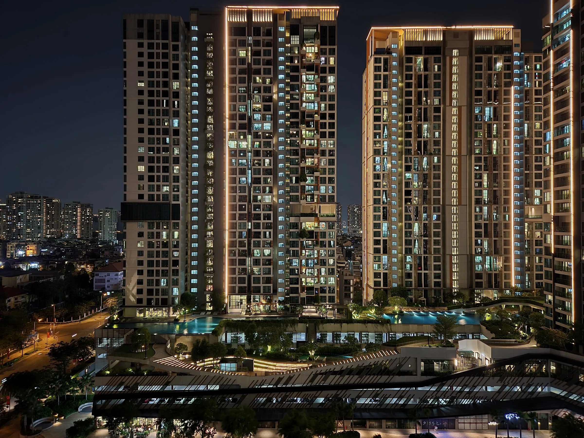 Illuminated residential high-rise towers at night above a landscaped courtyard and pool