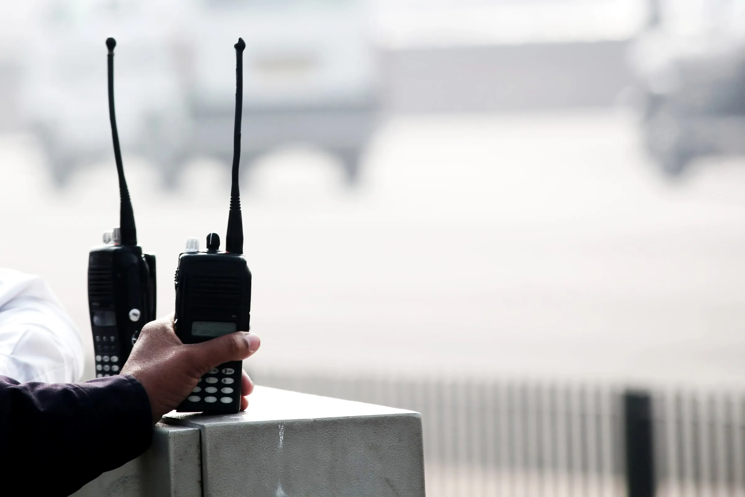 Two handheld radios standing upright on a concrete ledge, with a blurred figure behind