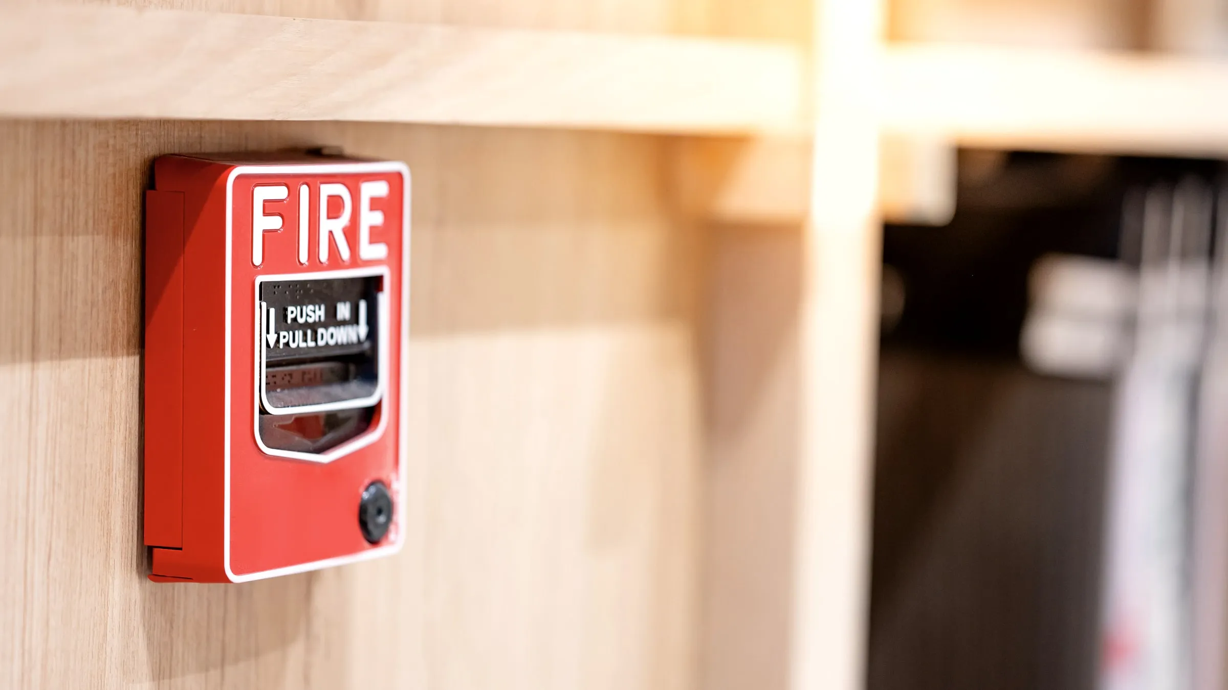 Hand pulling down the handle of a red fire alarm pull station mounted on a grey wall
