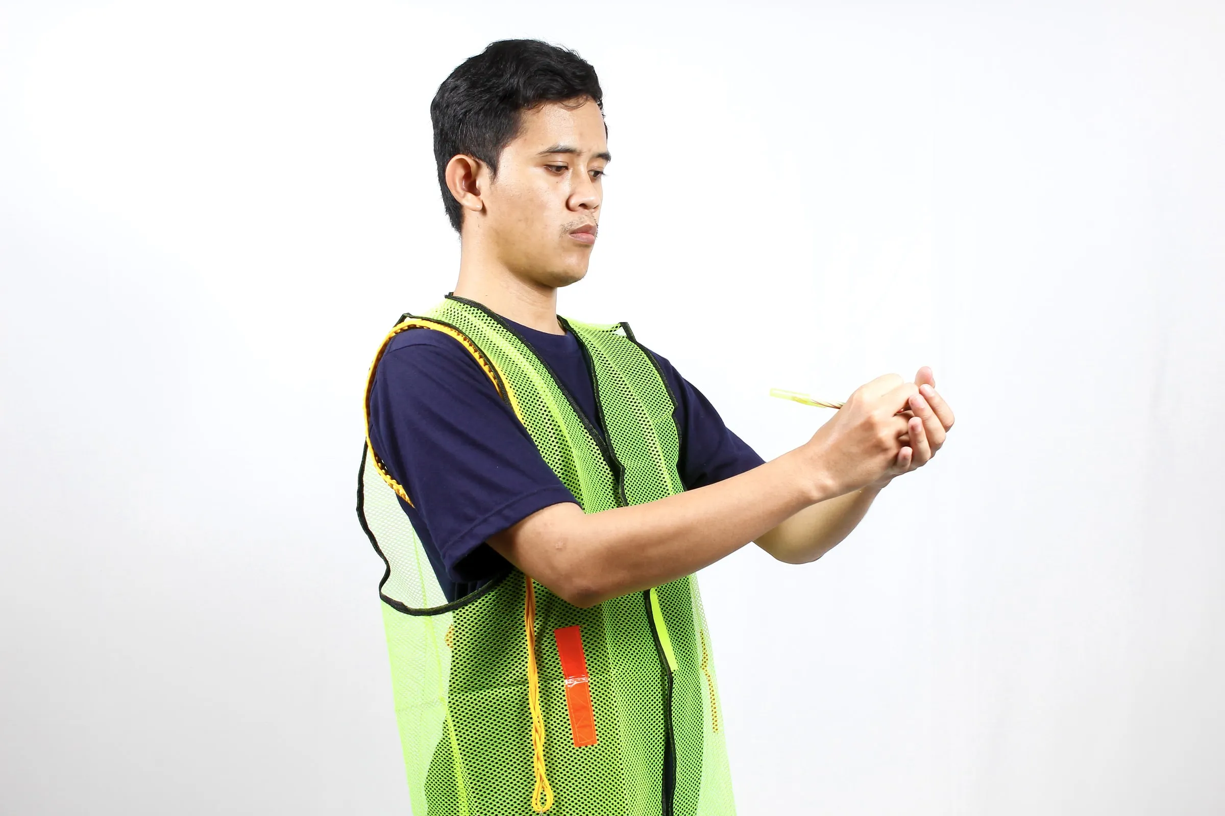 Young man in a green safety vest holding a tape measure against a white wall