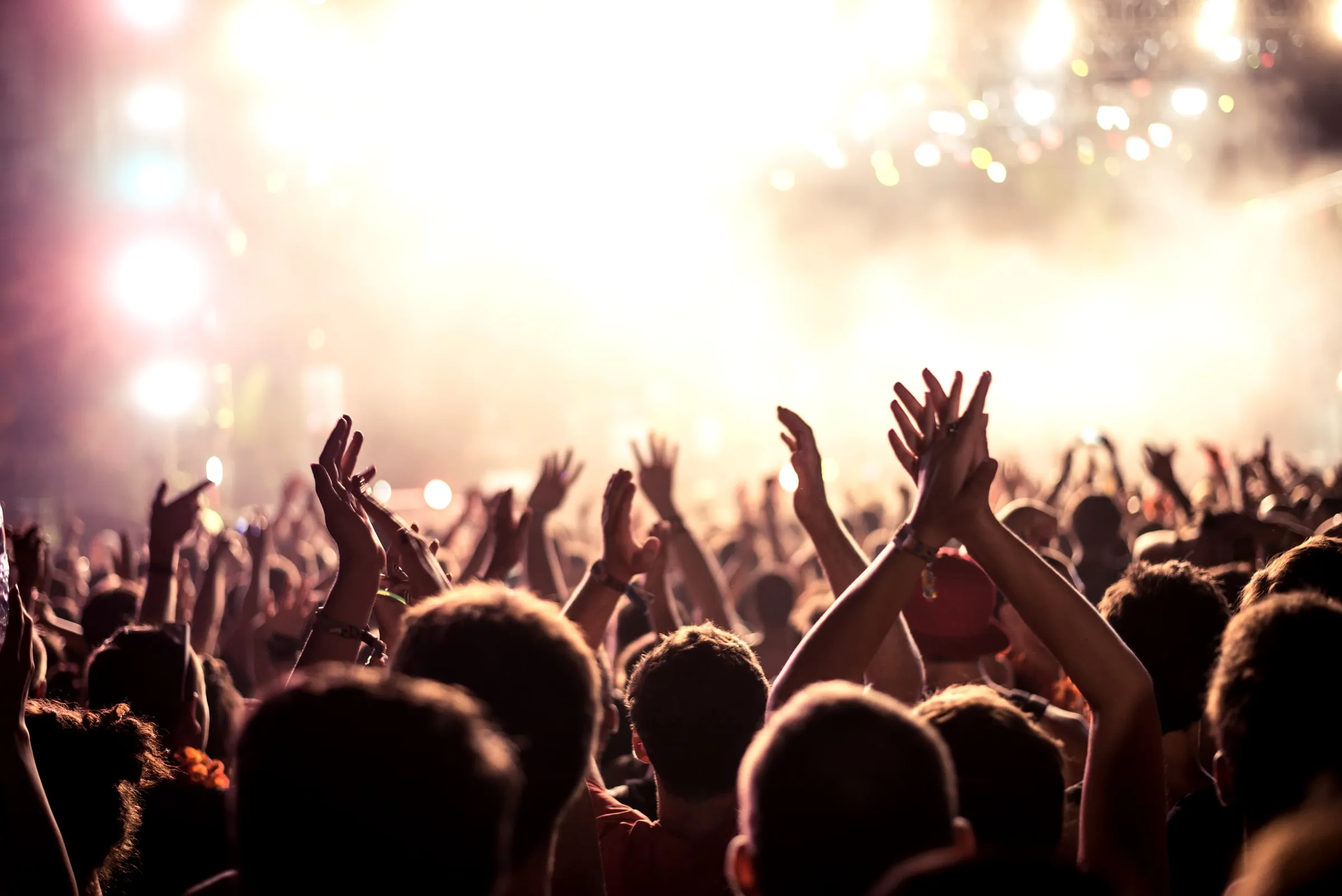 Concert crowd with raised hands under warm stage lights and haze