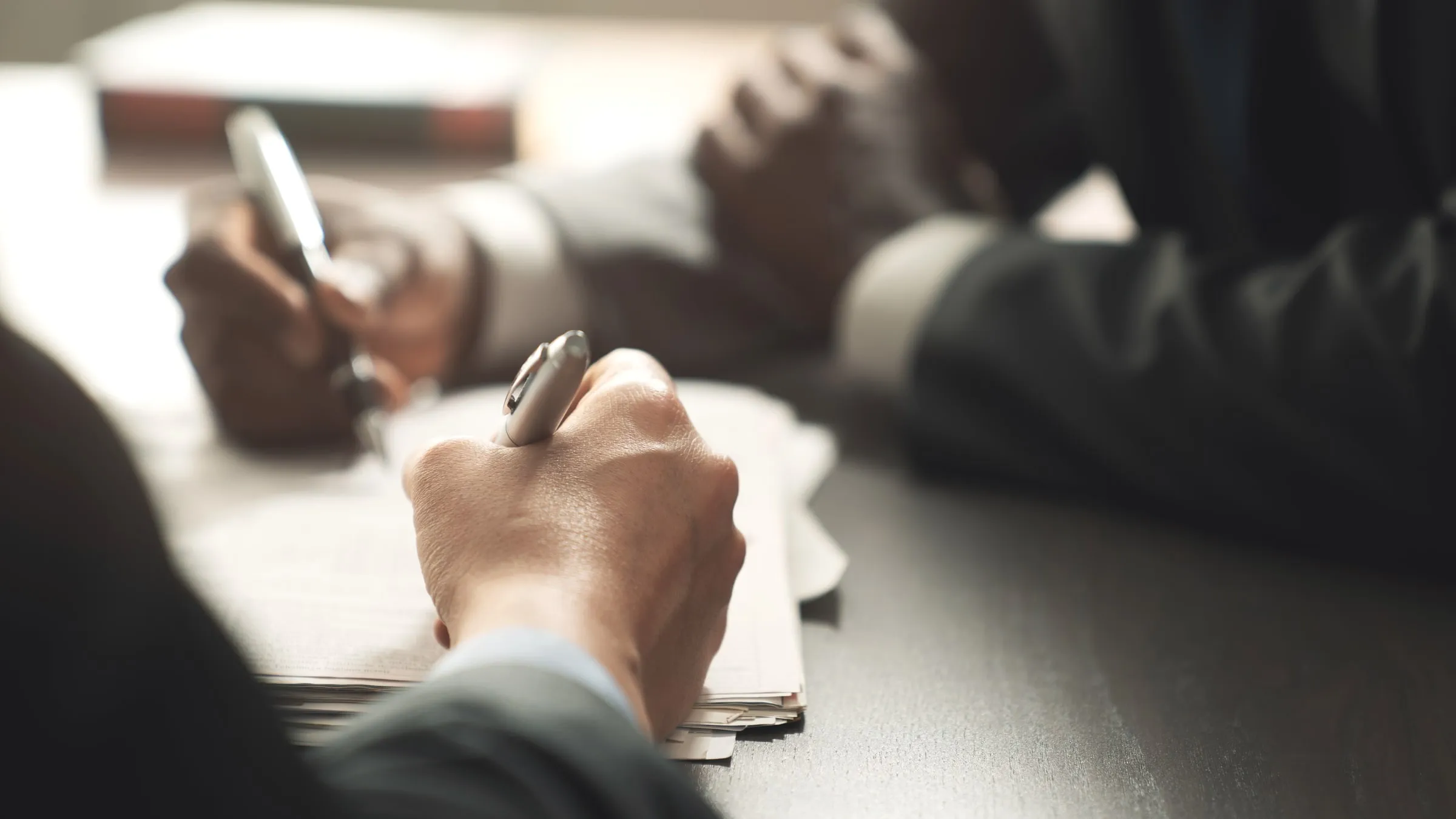 Close-up of two people's hands over documents on a desk, one writing with a pen
