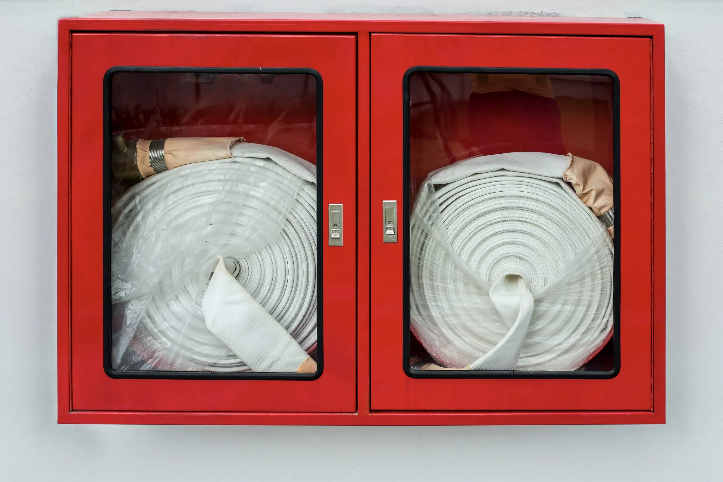Red wall cabinet with two coiled fire hoses behind glass doors