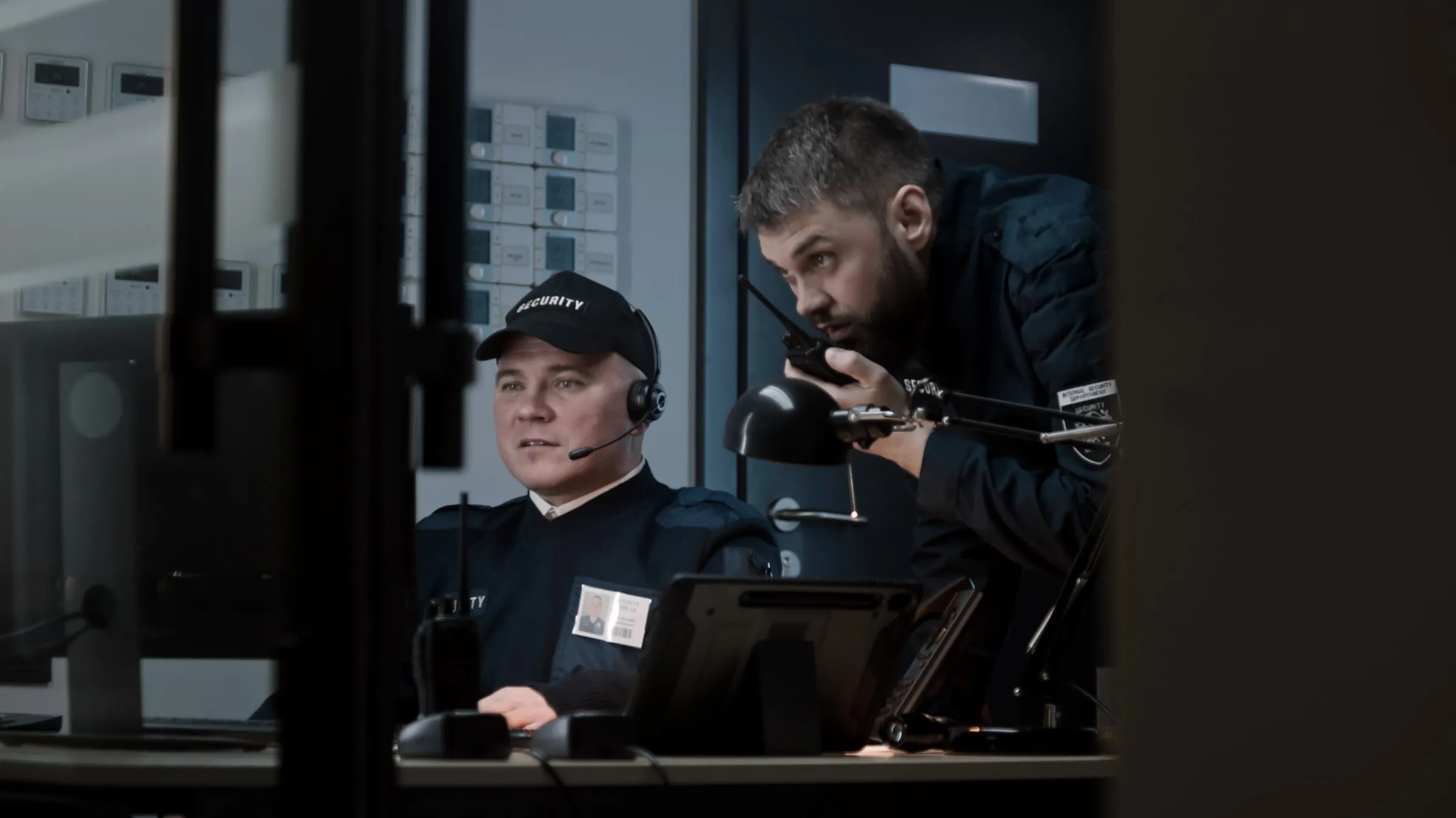 Two security officers in a dark control room, one on the phone and one looking at a screen