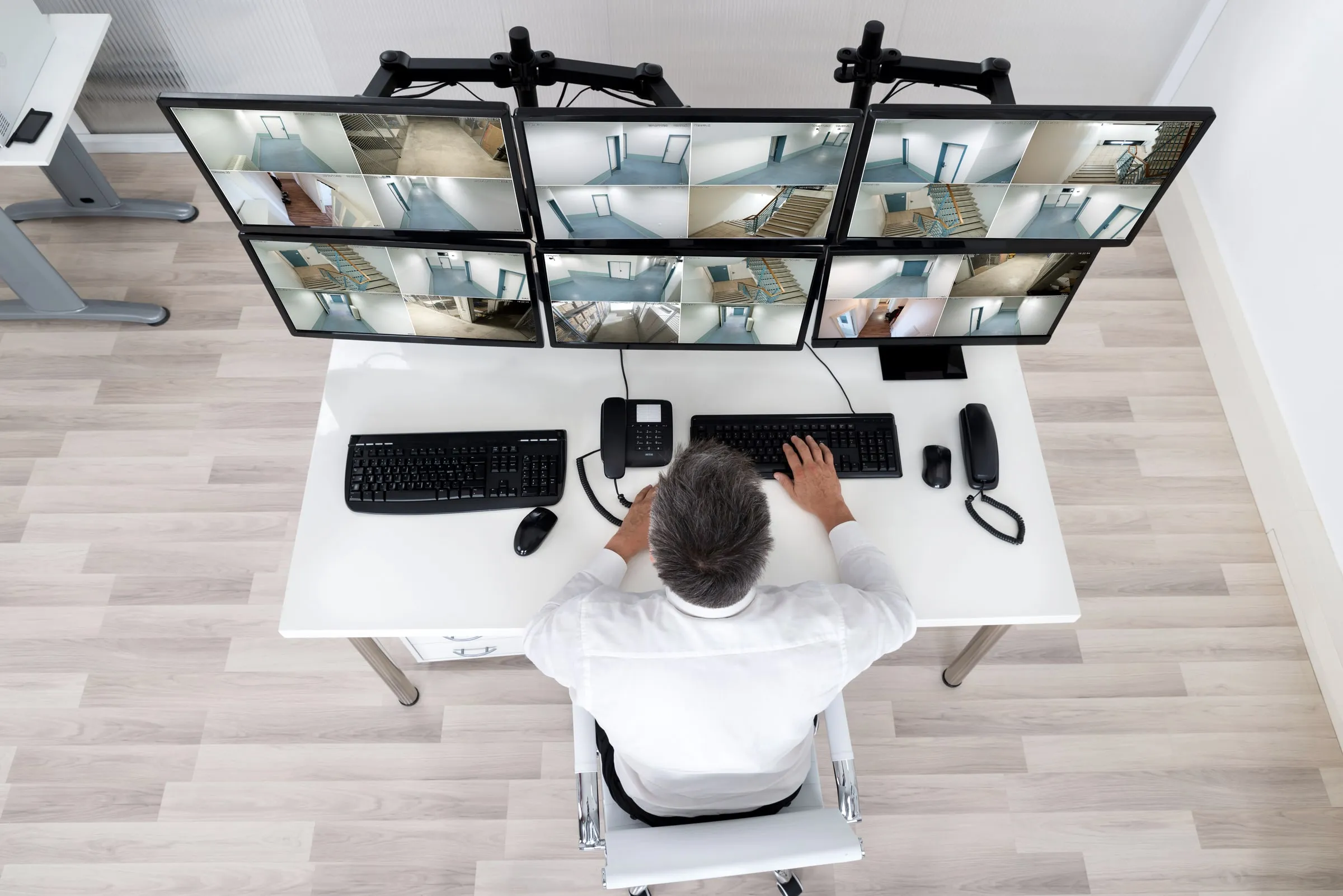 Overhead view of an operator at a desk with three monitors showing camera feeds