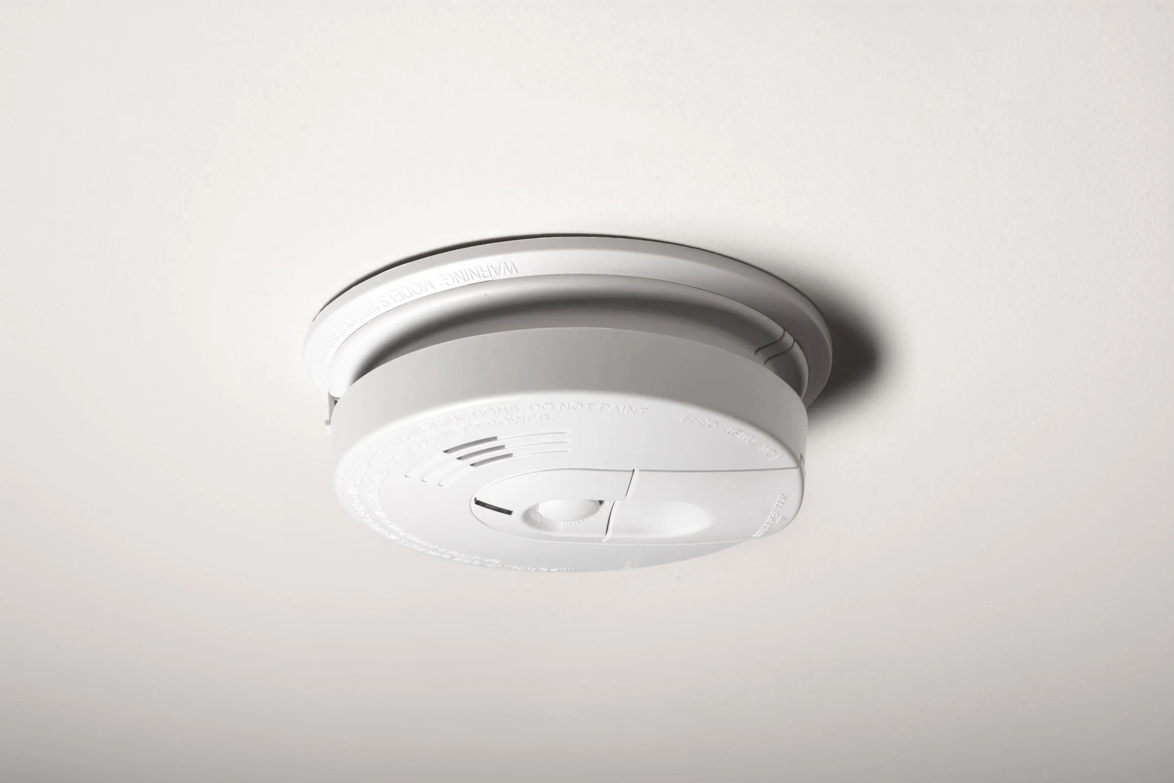 Round white smoke detector mounted on a plain ceiling