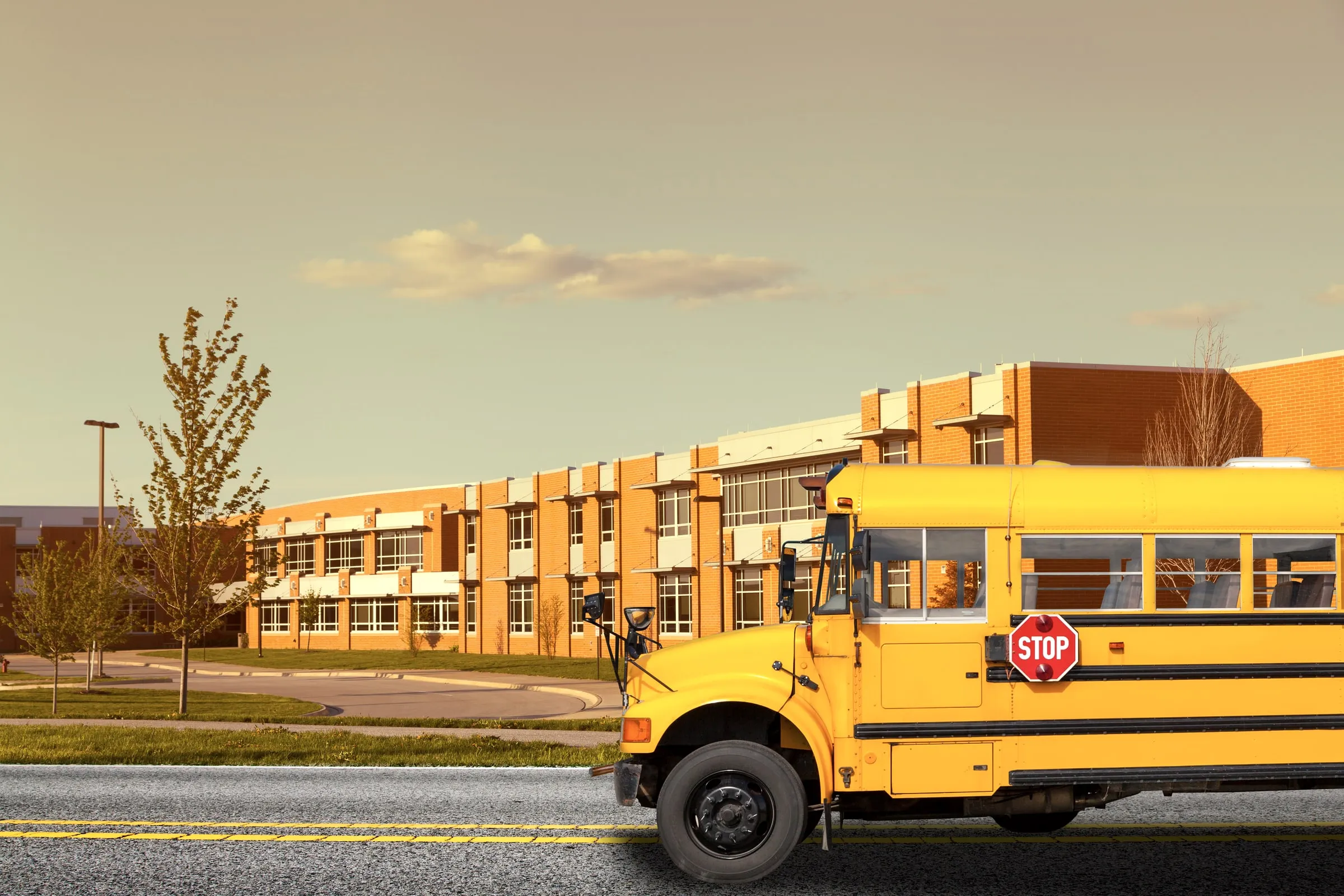 Yellow school bus with its stop sign extended in front of a brick school building at sunset