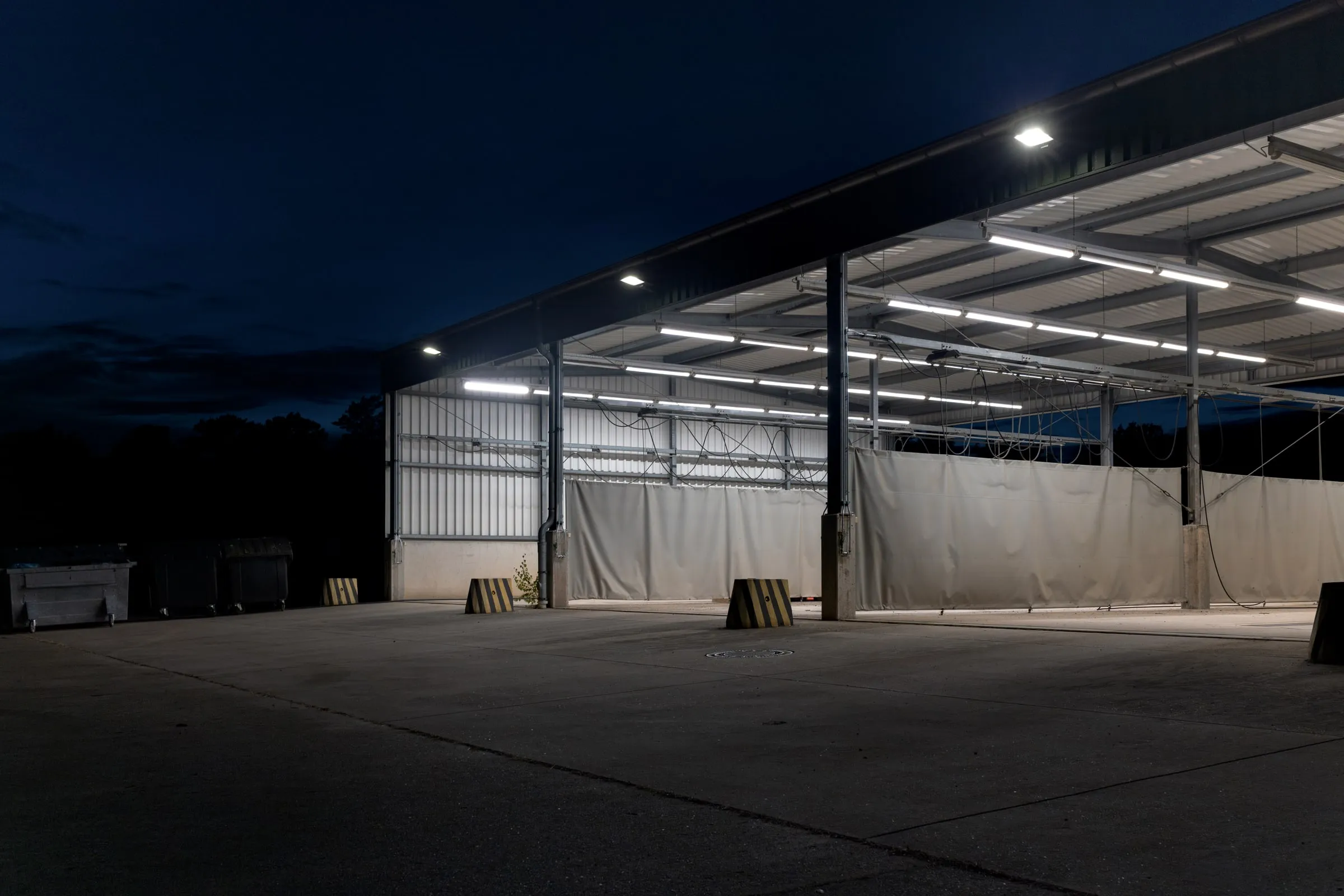 Empty warehouse yard at night with dock doors lit under a long canopy