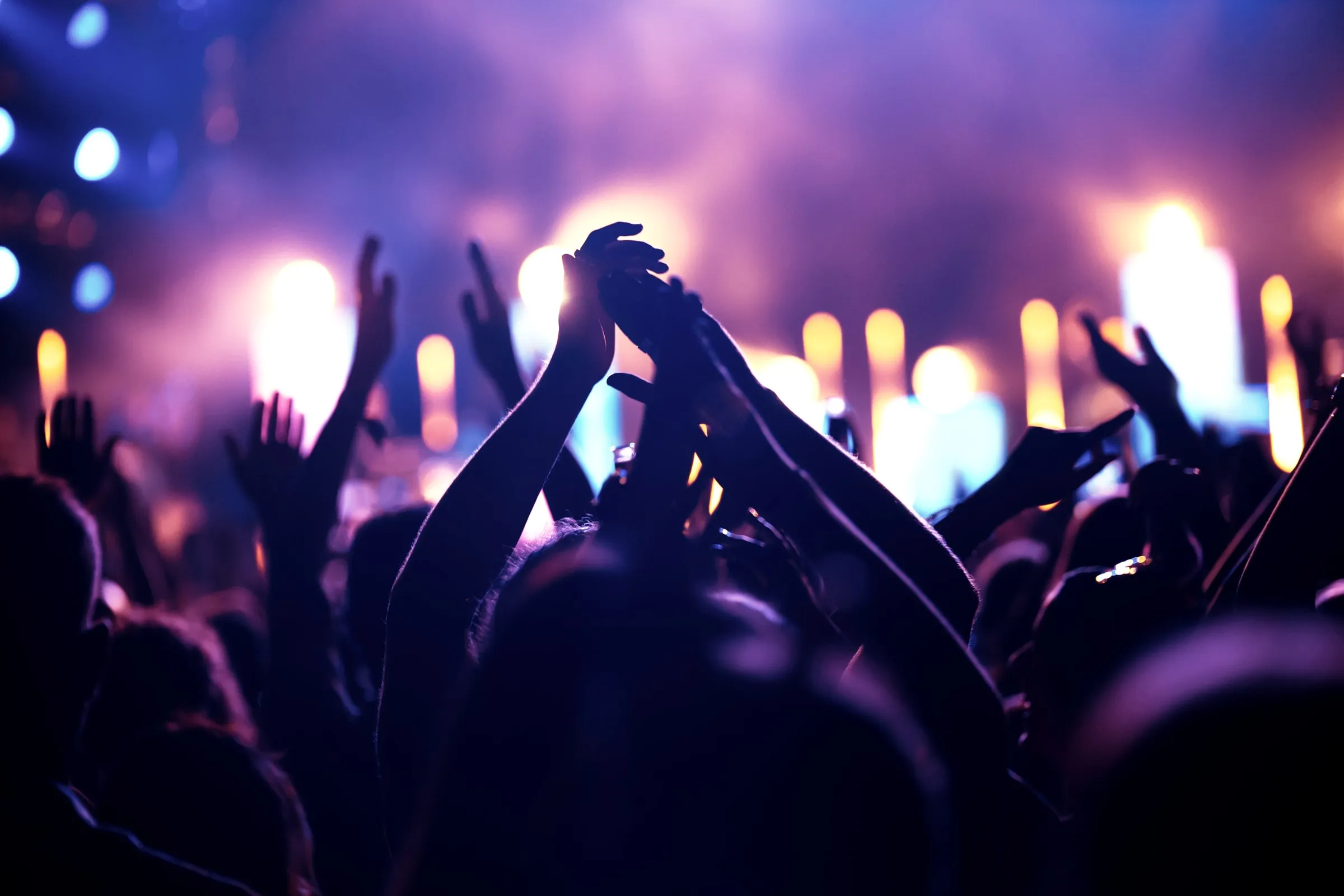 Crowd at a concert with hands raised under purple and blue stage lights
