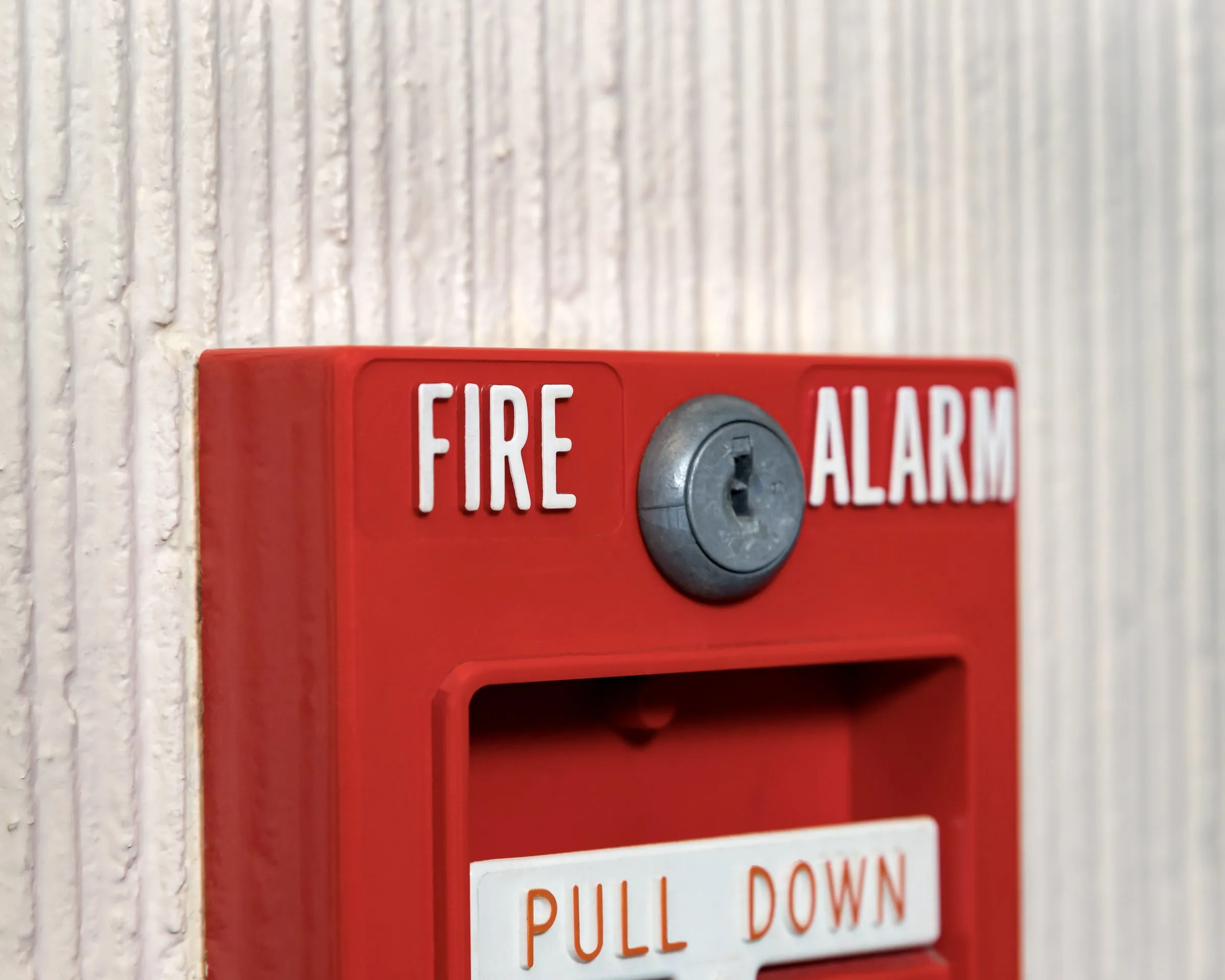 Red fire alarm pull station with a clear cover on a light wall