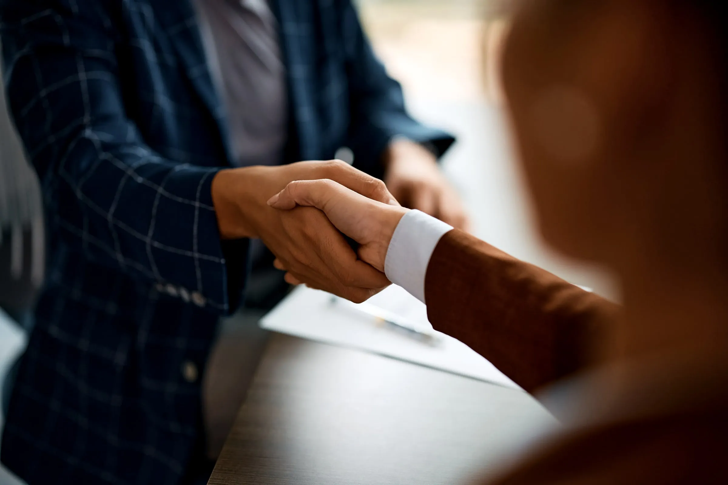 Close-up of two people shaking hands, one in a dark checked jacket, in a bright office