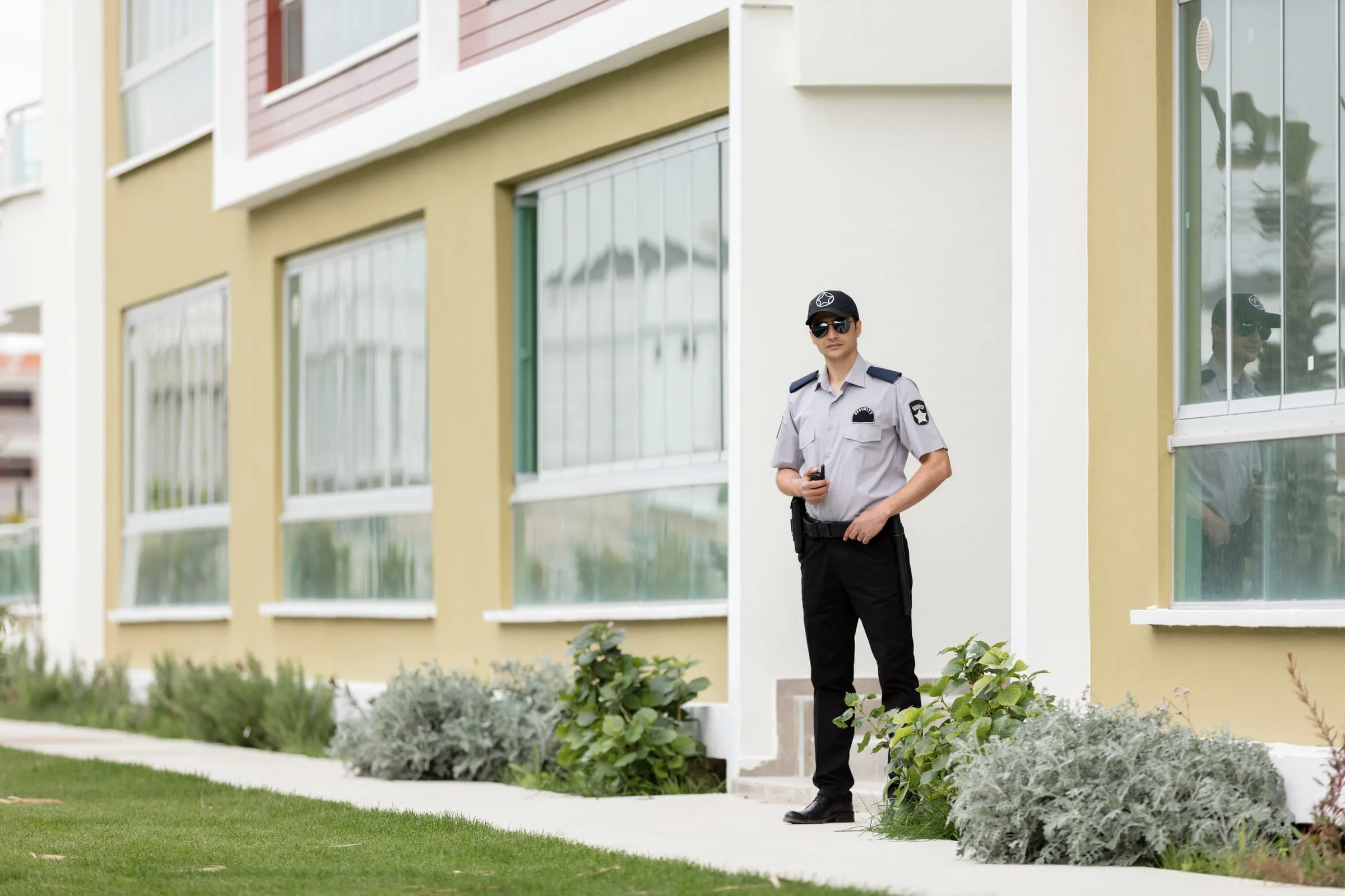 Security officer in a white shirt and dark trousers standing on a lawn in front of a modern apartment building