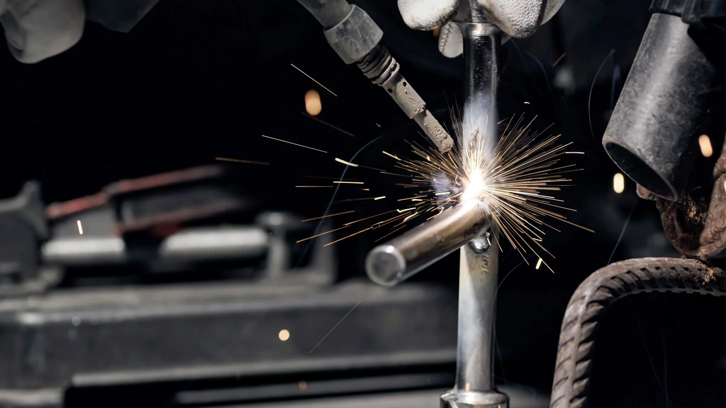 Welder in a protective mask working a torch on steel, with a shower of bright sparks against a dark workshop