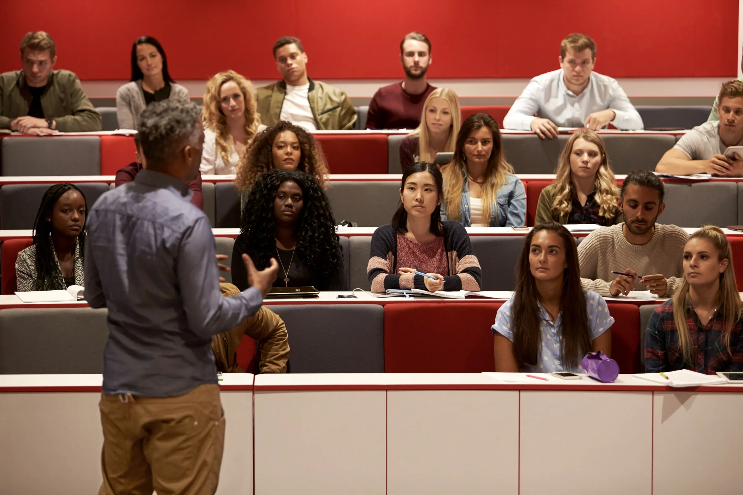 Instructor at the front of a tiered lecture room addressing rows of adult students
