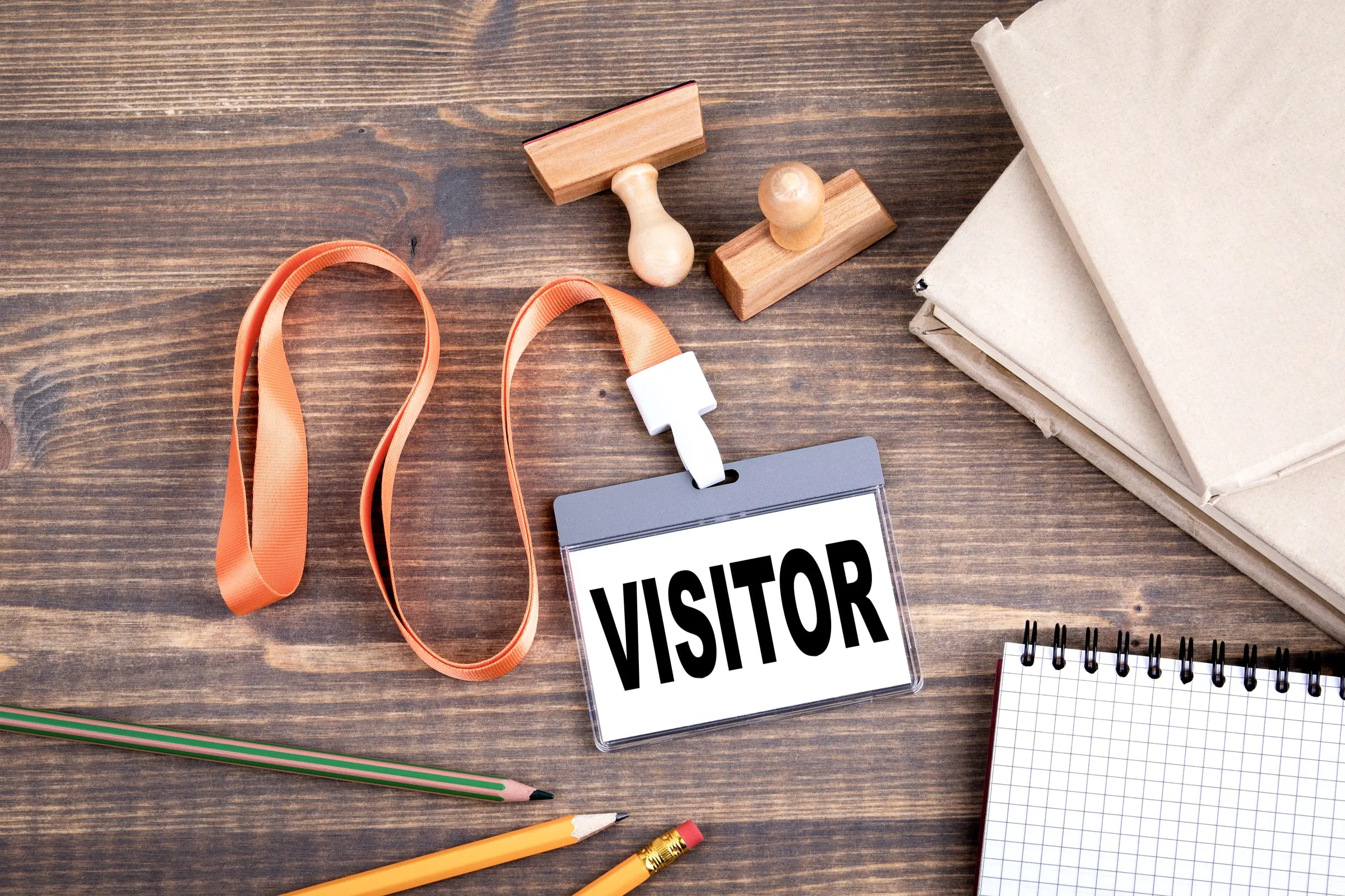 Visitor badge with a yellow lanyard lying on a wooden desk beside a notebook and pencils