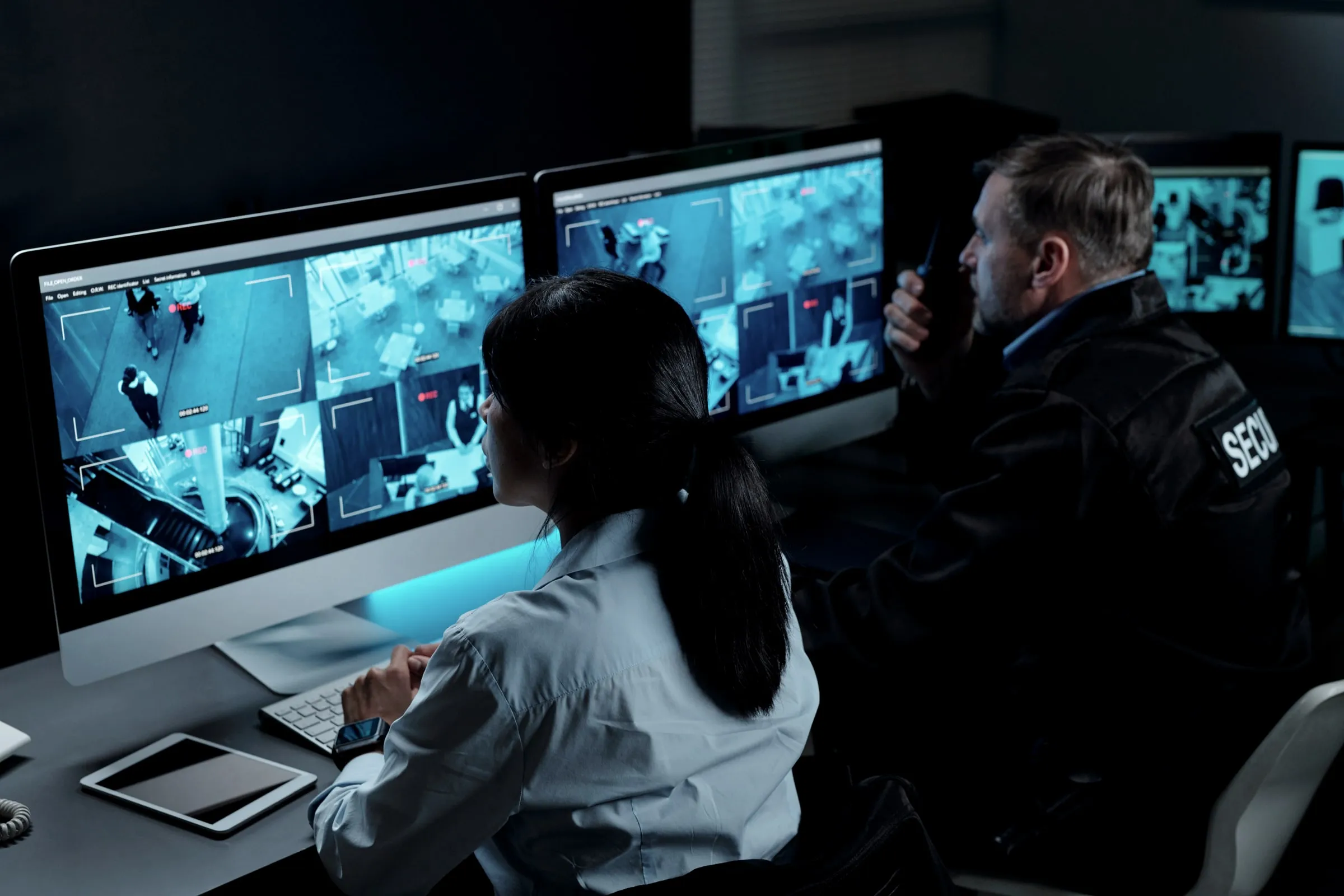 Two security operators at a desk with camera monitors, one on the phone and one looking over