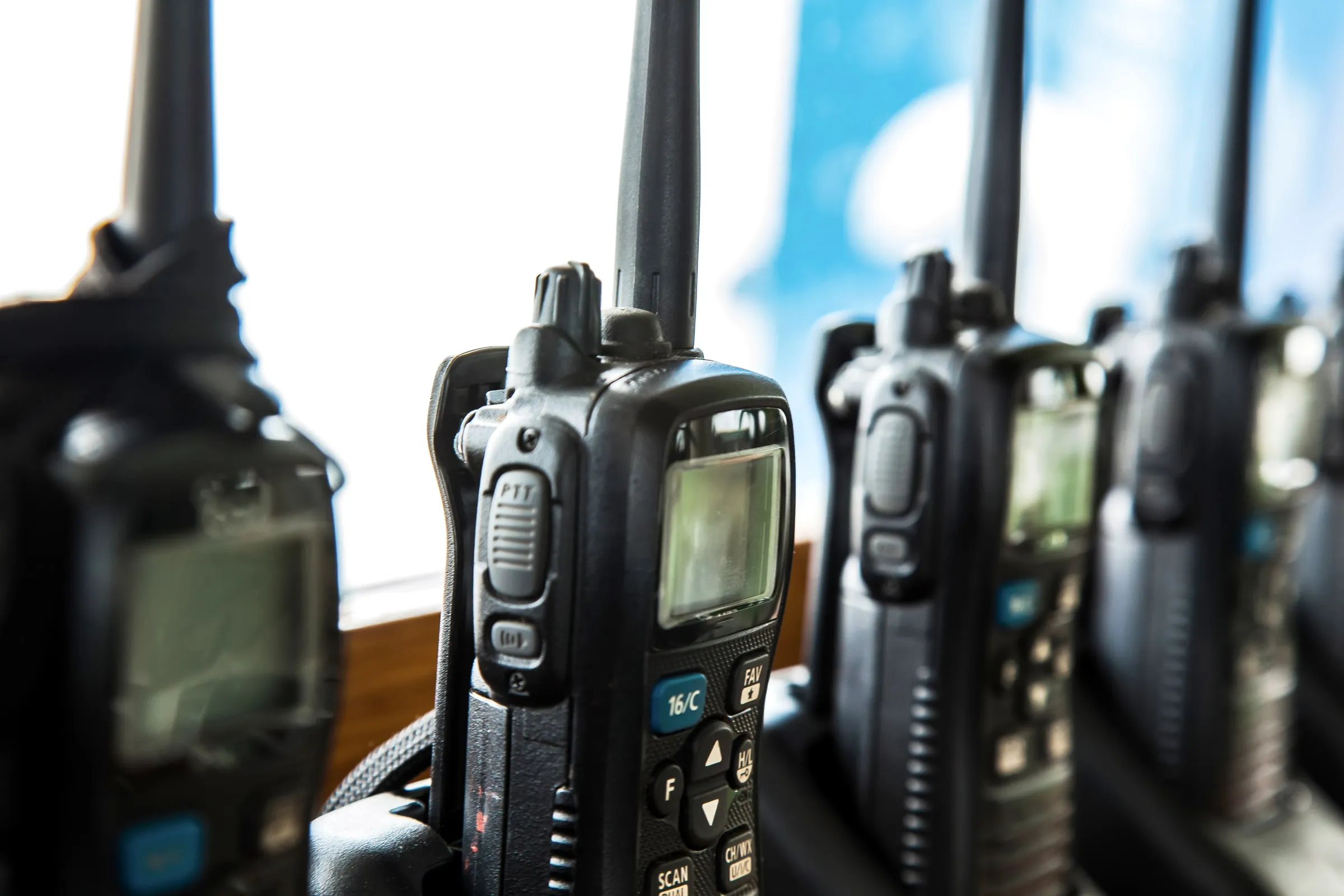 Row of handheld radios standing upright in chargers on a shelf