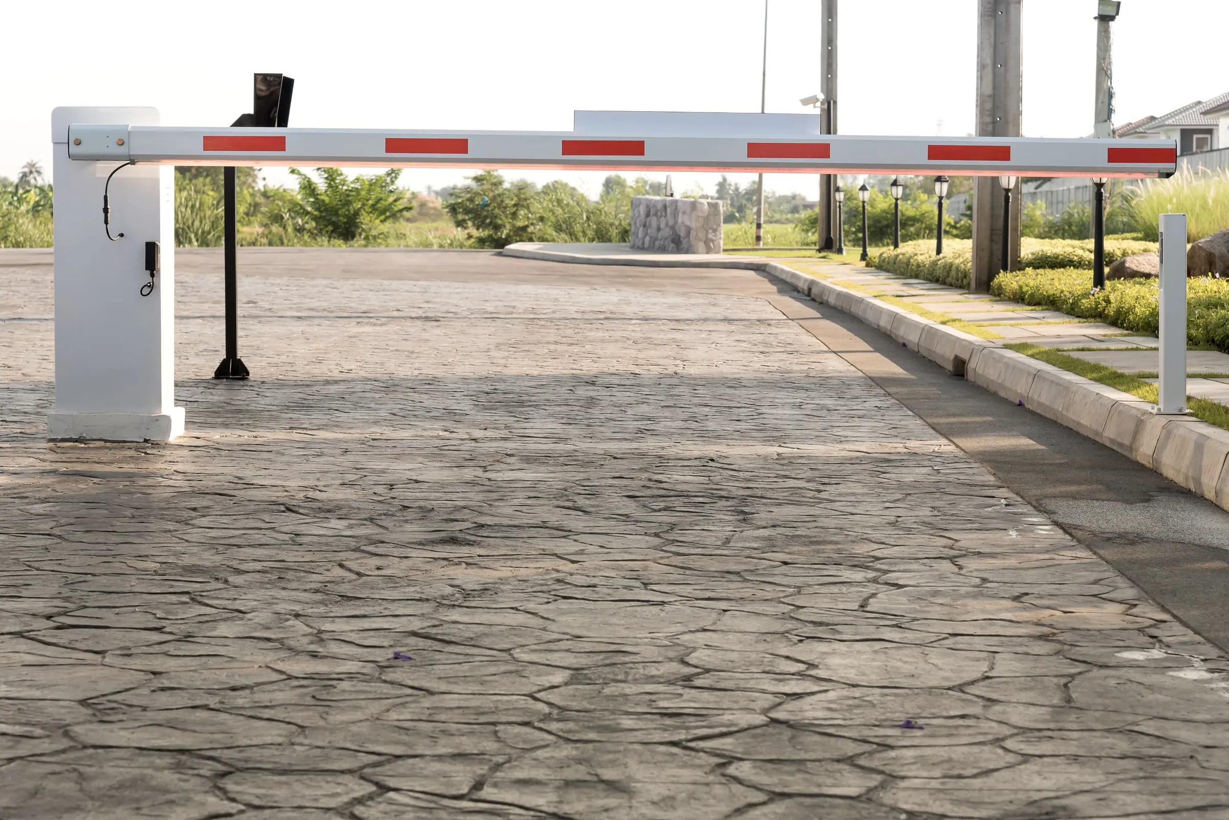 White barrier arm with red stripes lowered across a paved entrance lane beside a small booth