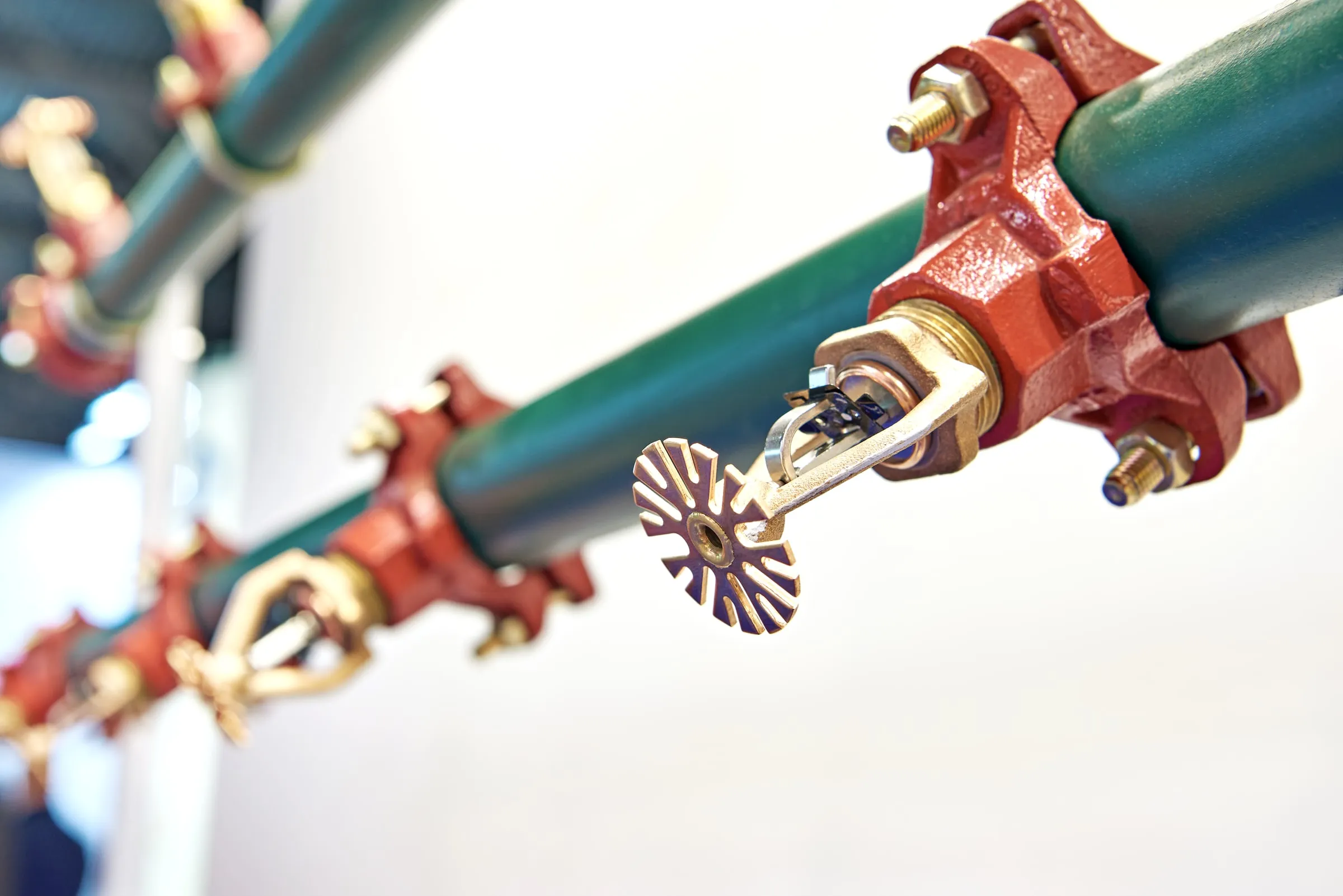 Red fire sprinkler pipe fittings and a control valve on a green pipe against a white wall