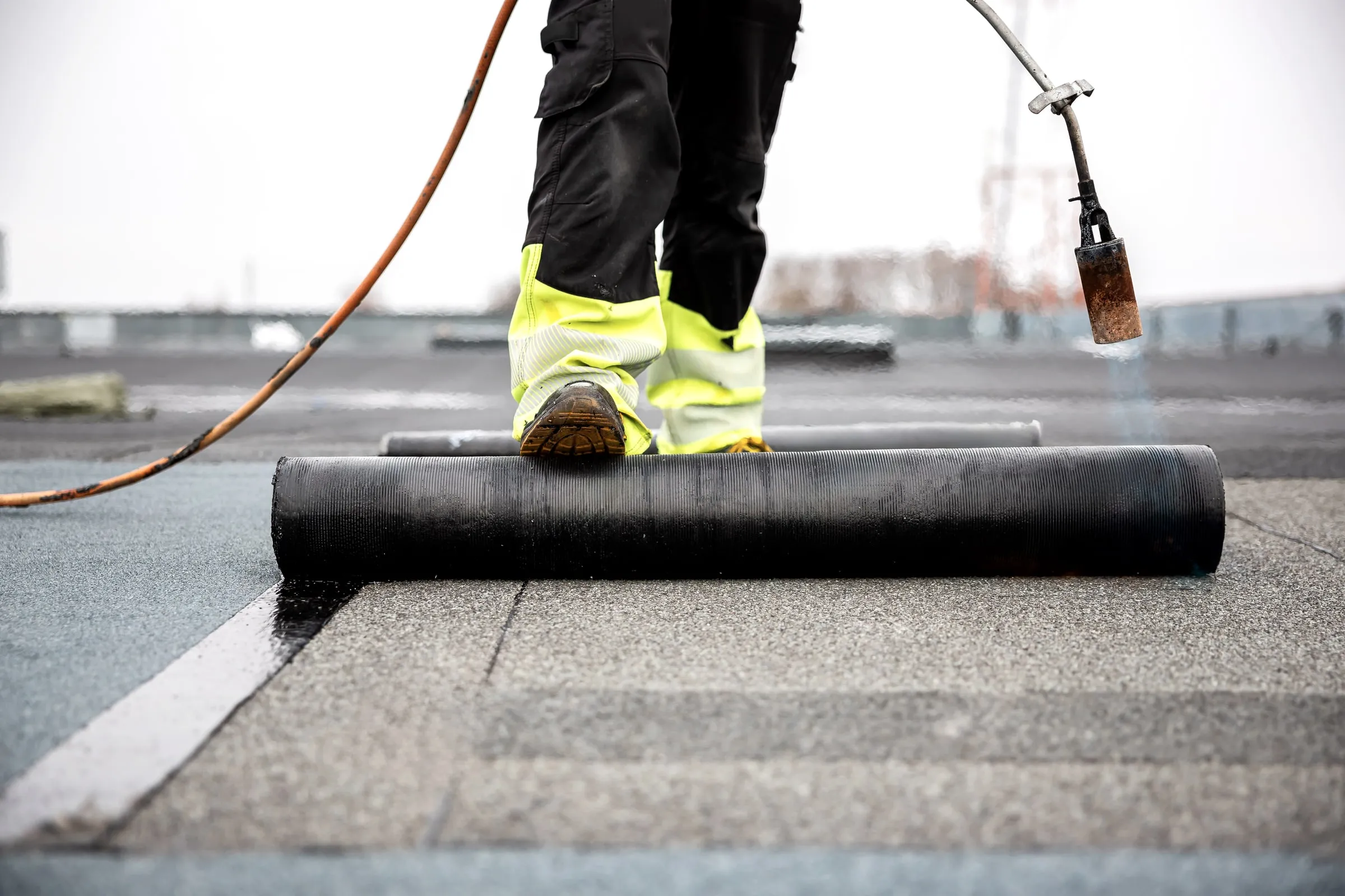 Roofer's boots and a torch beside a roll of membrane on a flat roof
