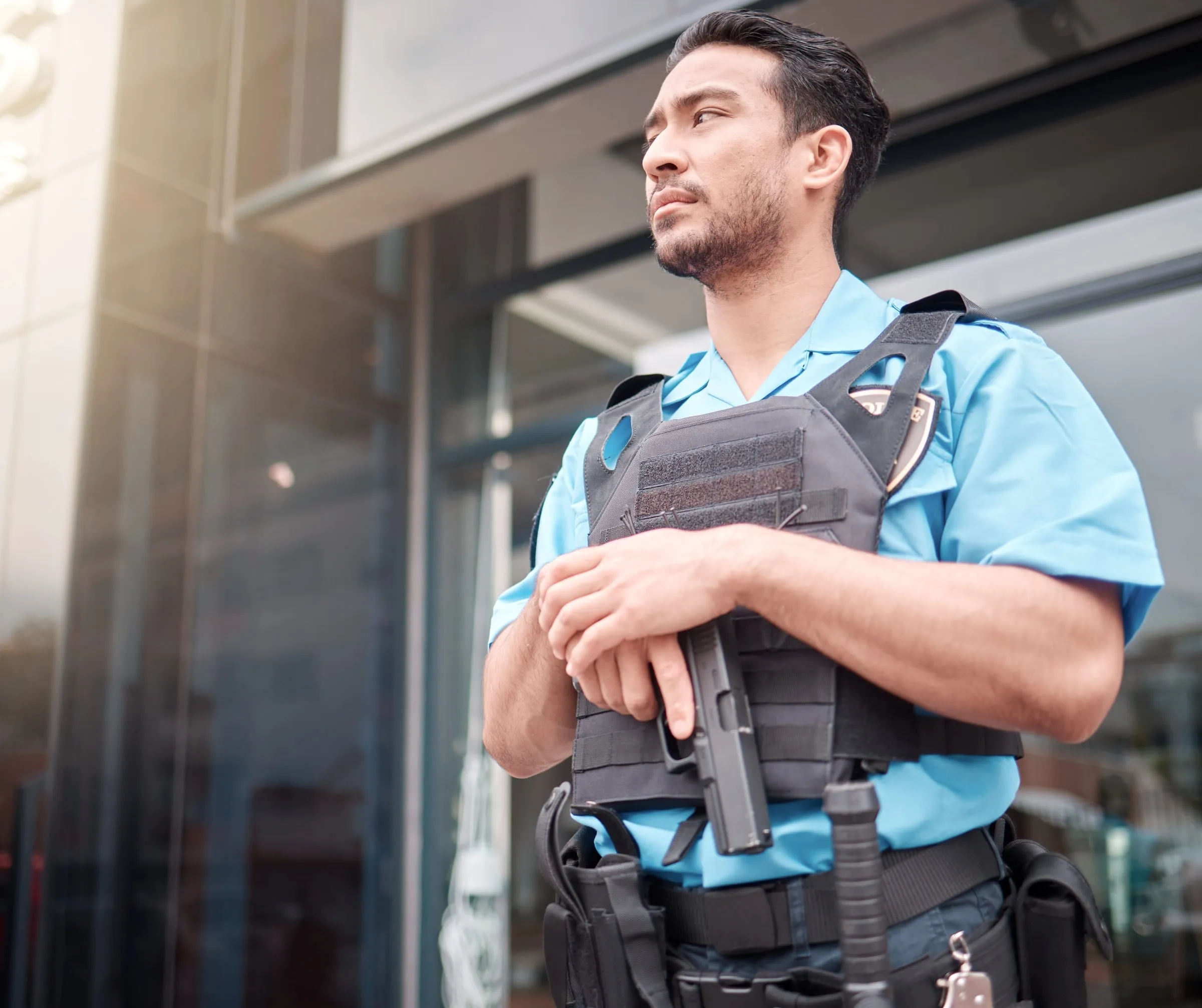Armed security officer in a tactical vest at a building entrance
