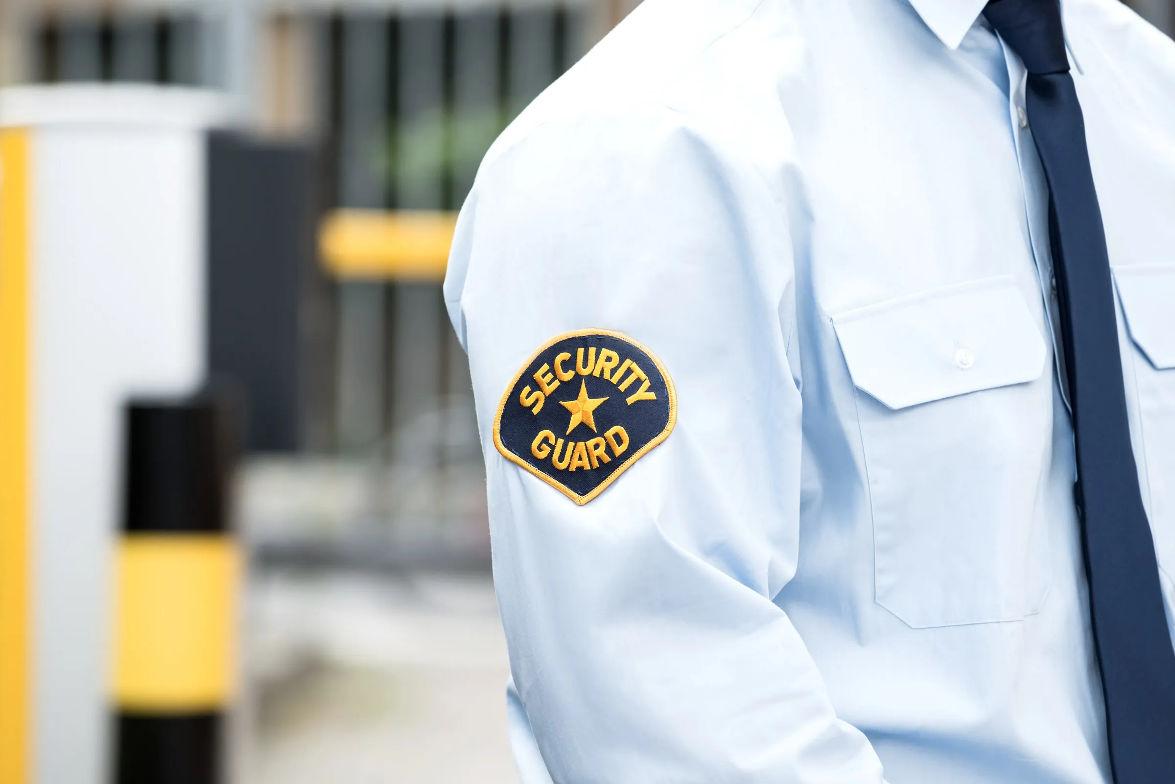 Close view of a white uniform shirt with a SECURITY GUARD shoulder patch beside a yellow-and-black bollard