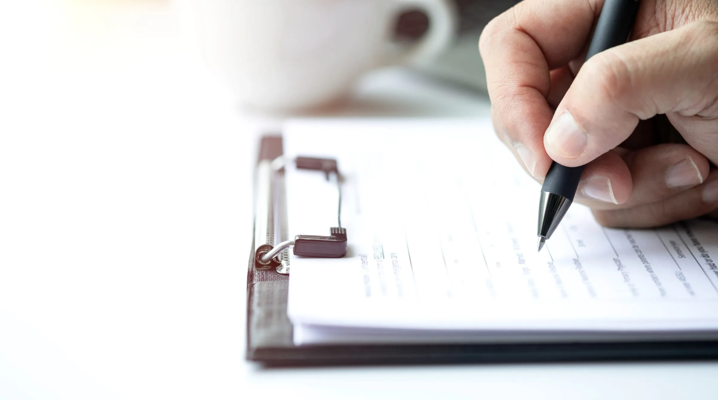 Hand holding a pen filling in a form on a clipboard, seen close up