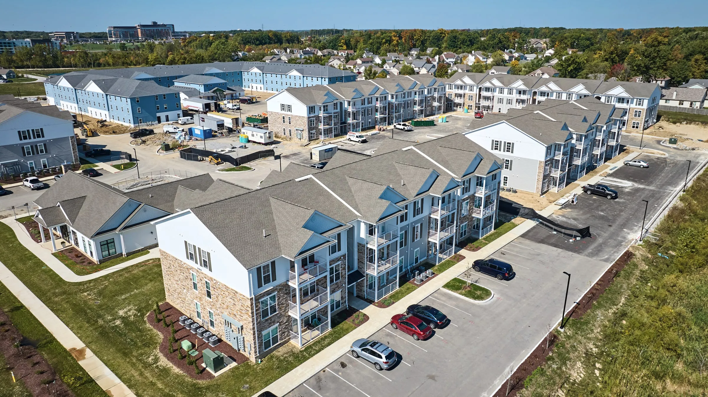 Aerial view of a new suburban apartment complex with stone and siding buildings, a clubhouse and freshly paved parking