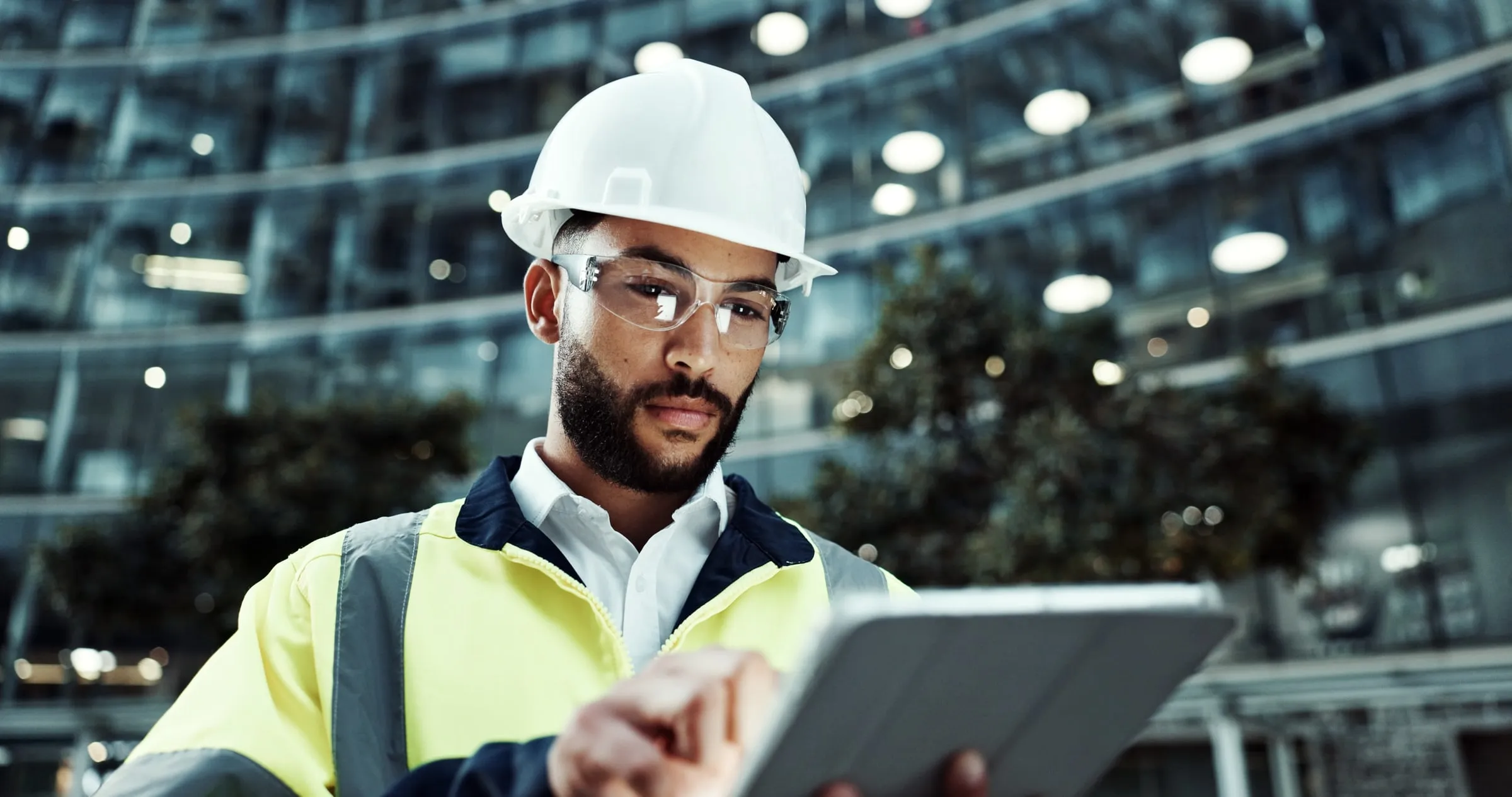 Fire watch inspector in a hard hat and hi-vis vest recording a site inspection on a tablet