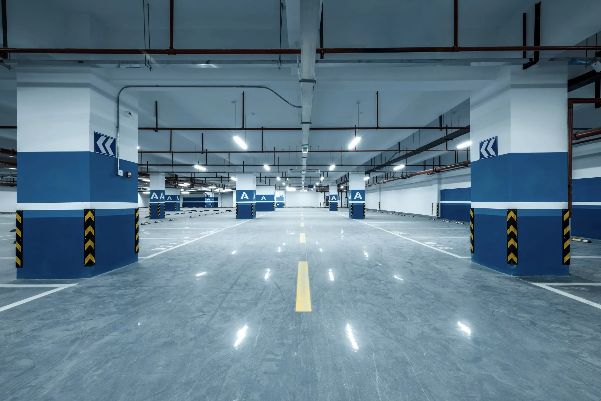 Empty multi-level parking garage interior with blue and white striped support columns, directional arrows and a polished concrete drive lane