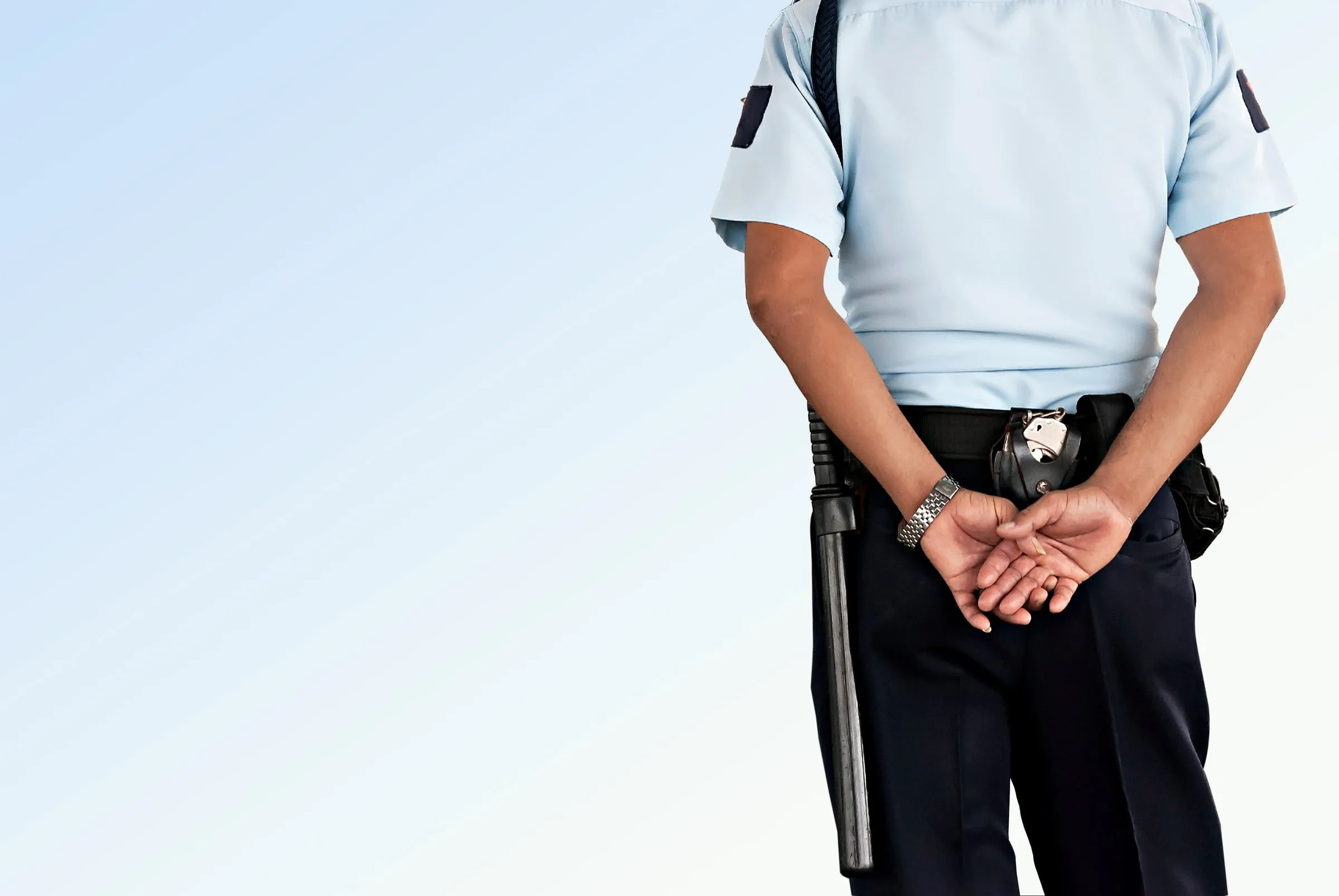 Man in a dark uniform holding a radio while looking at a wall of monitors showing multiple building interior camera feeds