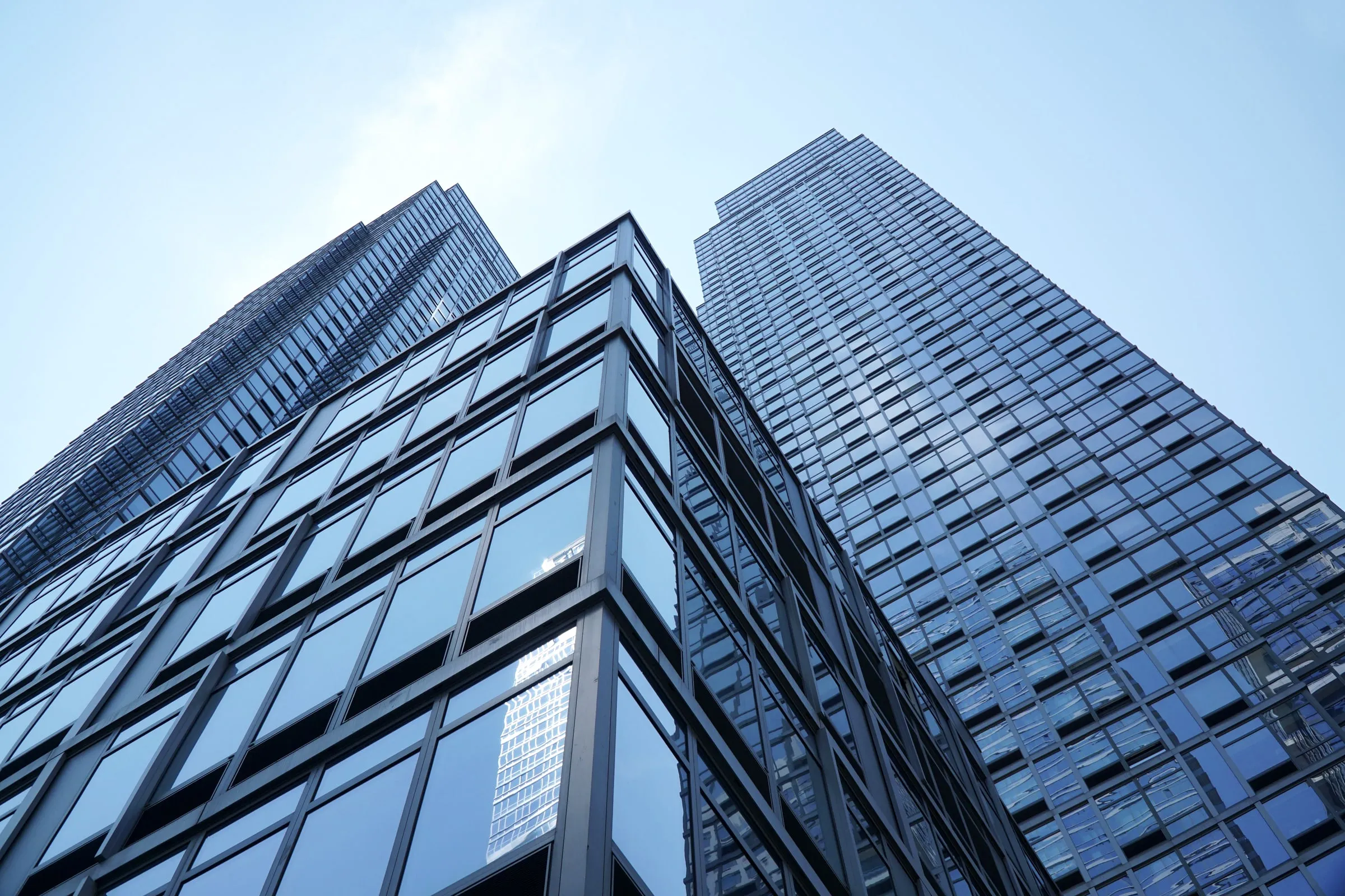Low-angle view of two glass office towers against a clear blue sky