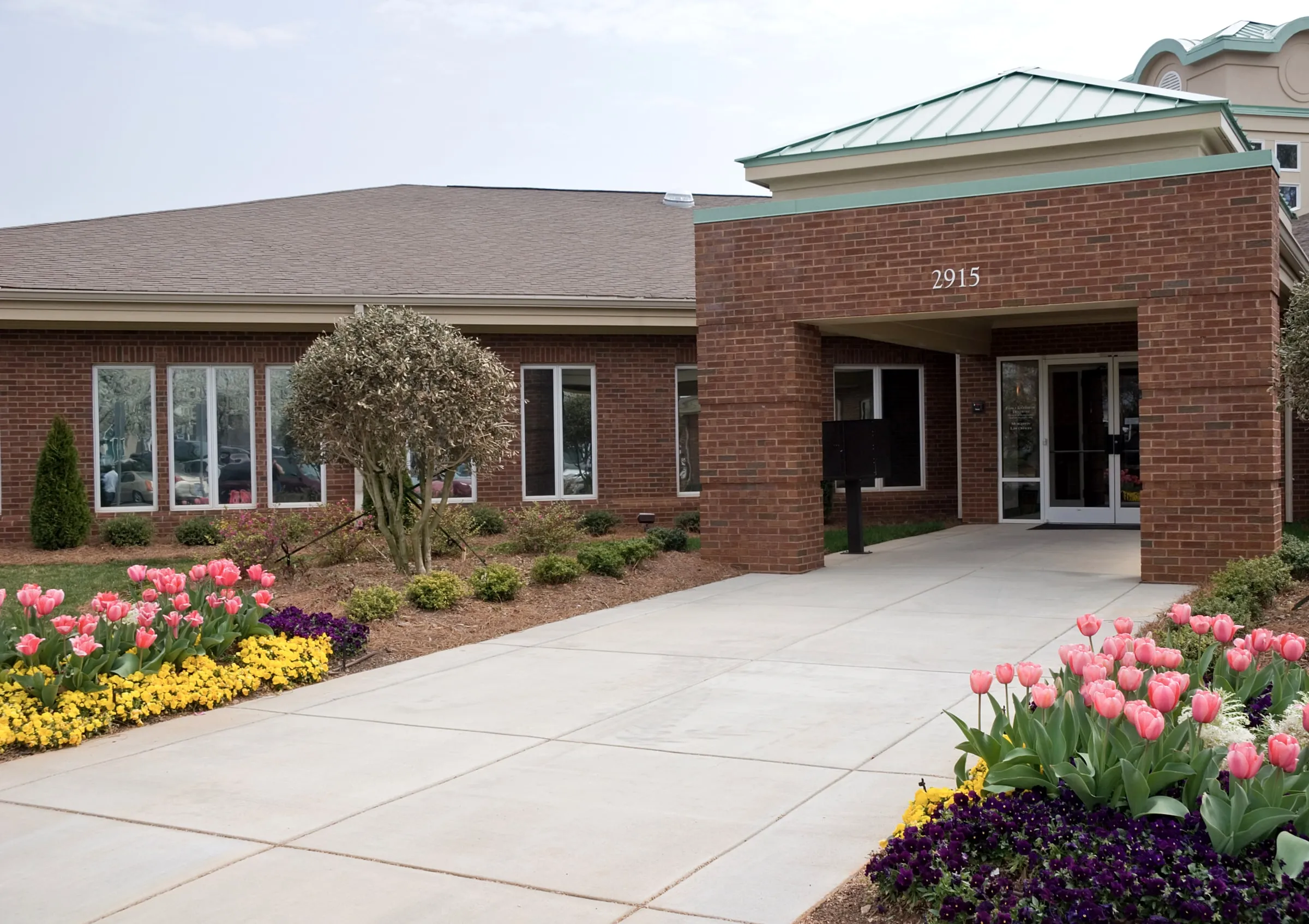 Single-story brick medical office building with a covered entrance, tulip and pansy beds and a wide concrete approach