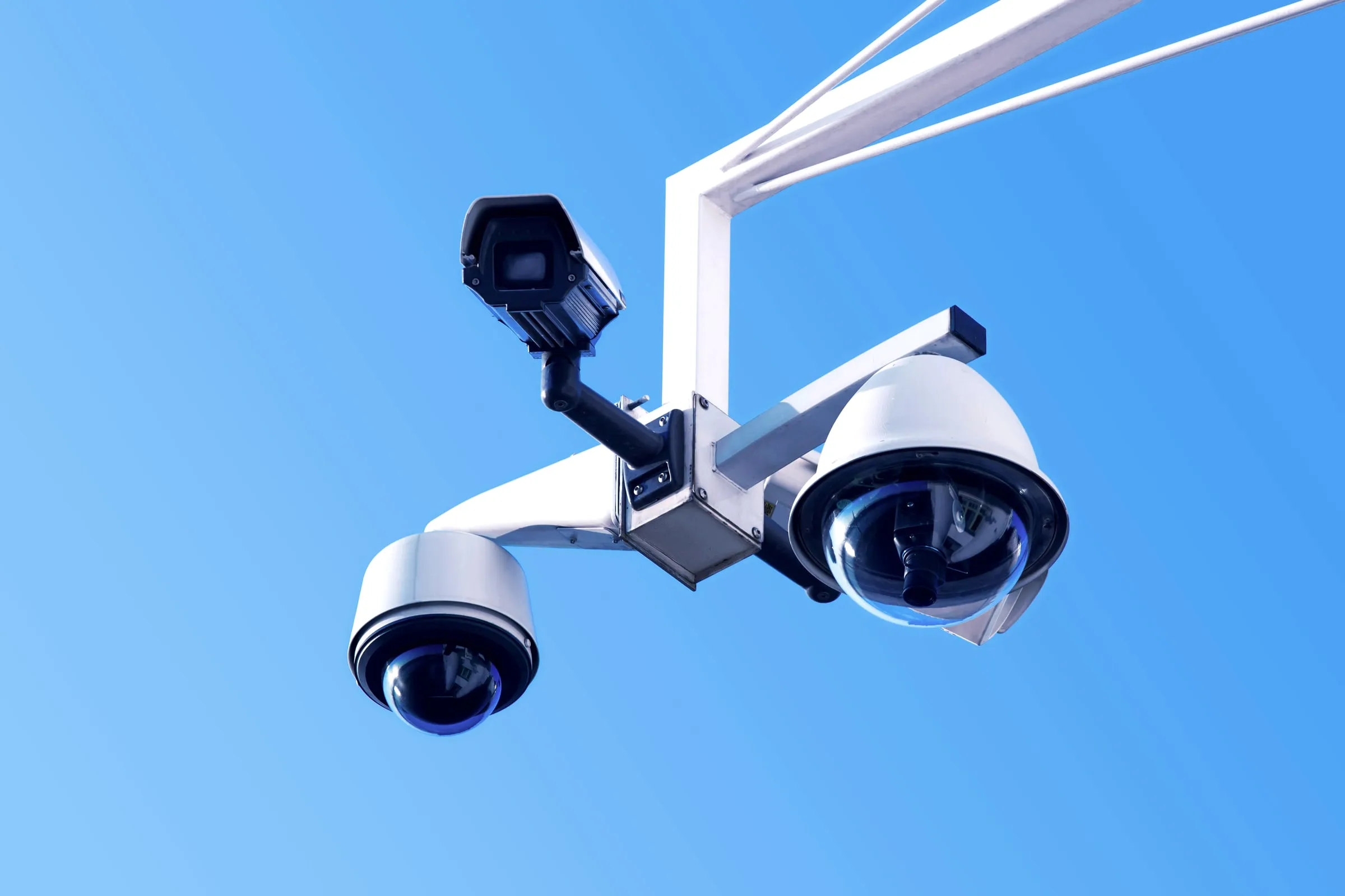 Two white outdoor security cameras mounted on a pole against a clear blue sky
