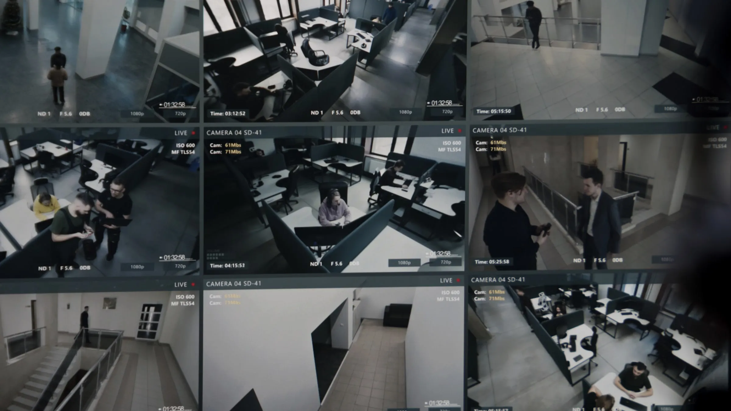 Grid of nine security camera monitor feeds showing office desks, a stairwell landing and a hallway, viewed on a wall-mounted screen