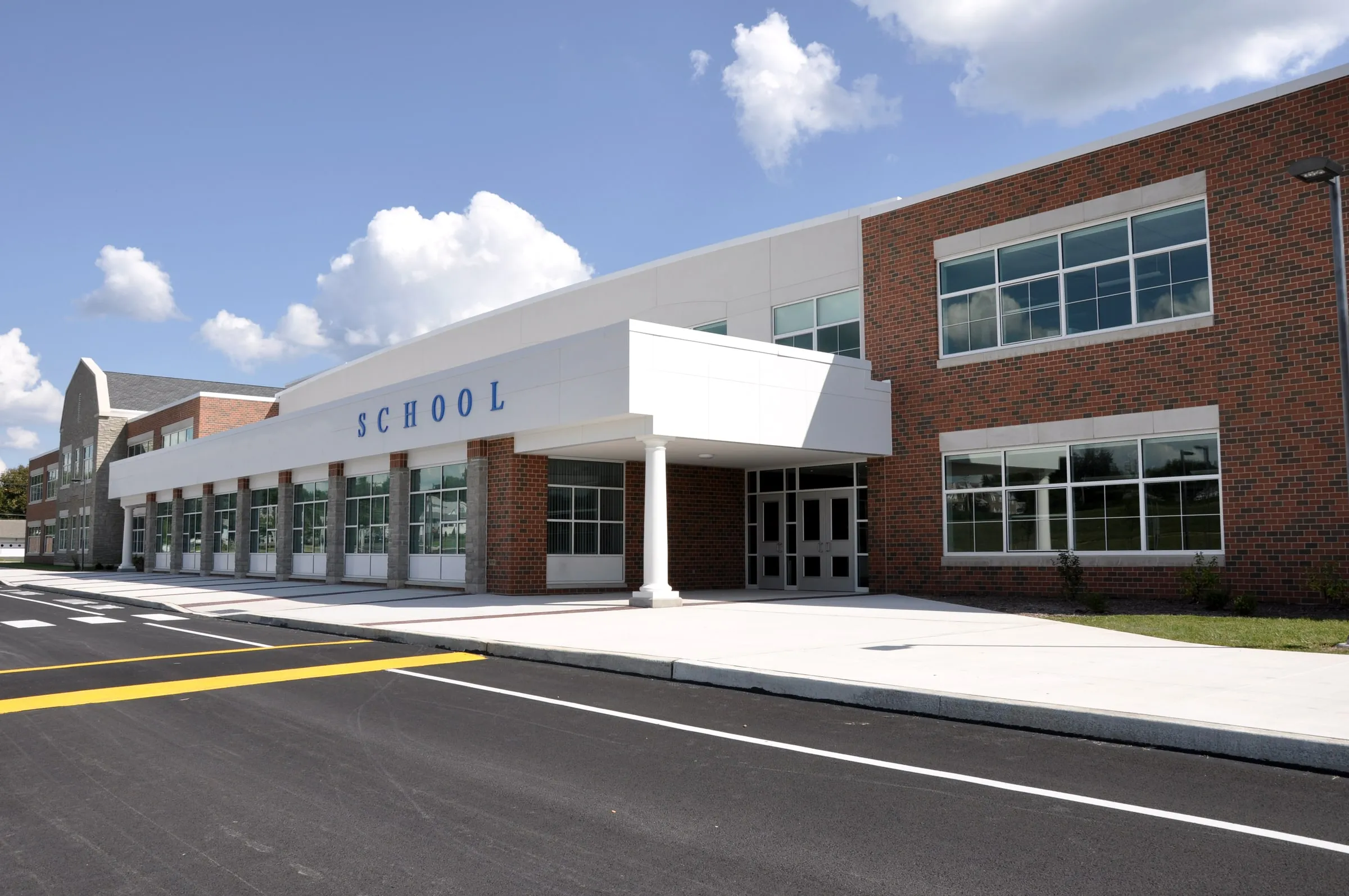 Single-story brick school building with a covered entrance and a SCHOOL sign, a crosswalk and empty parking lot in the foreground