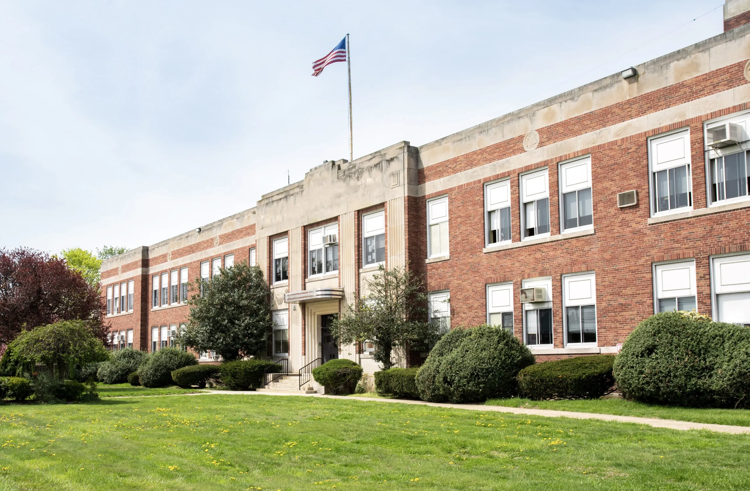 Two-storey red brick school building with white trim, an American flag and a lawn with trees