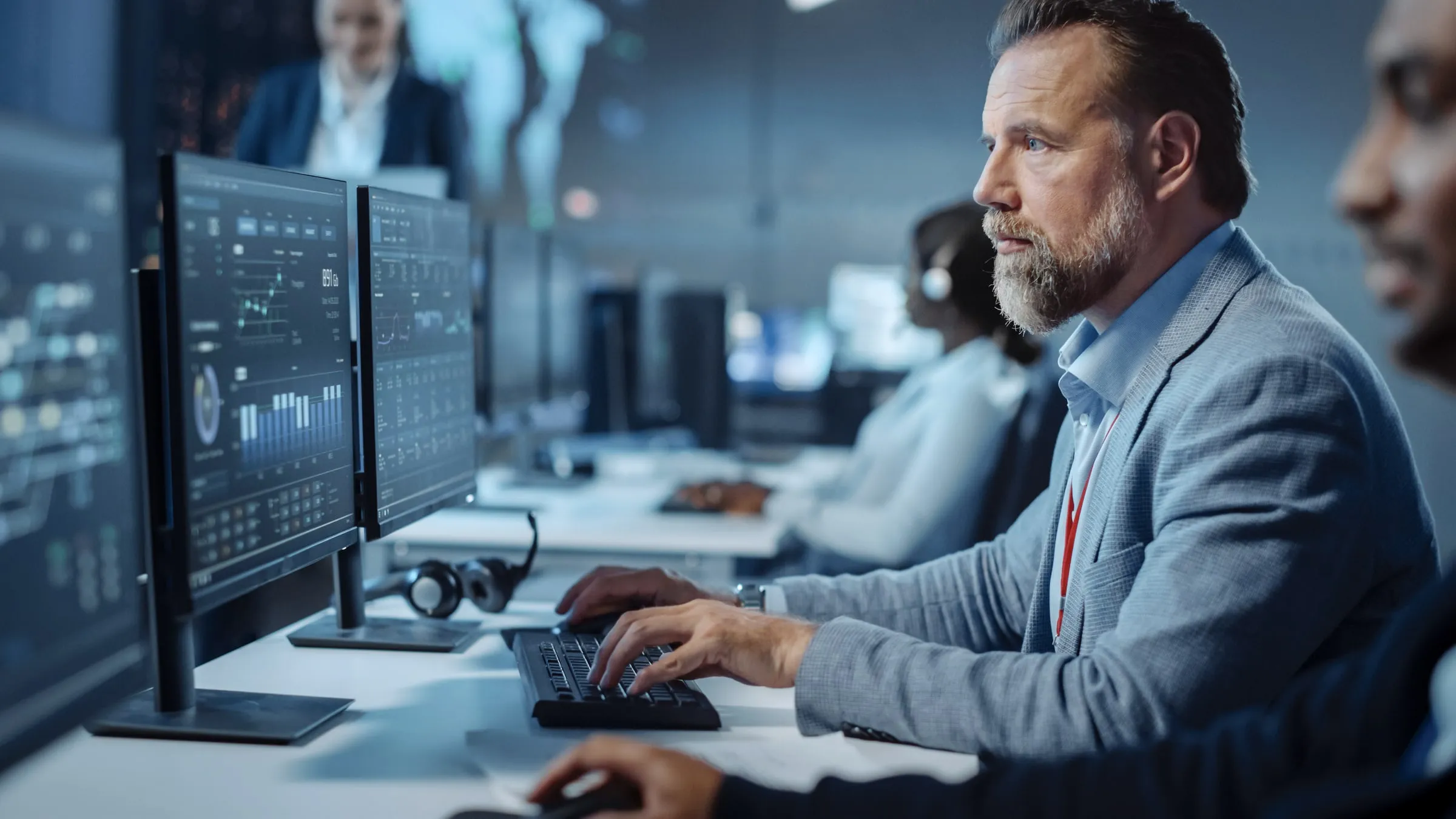 Man with a lanyard working at a bank of monitors in a control room