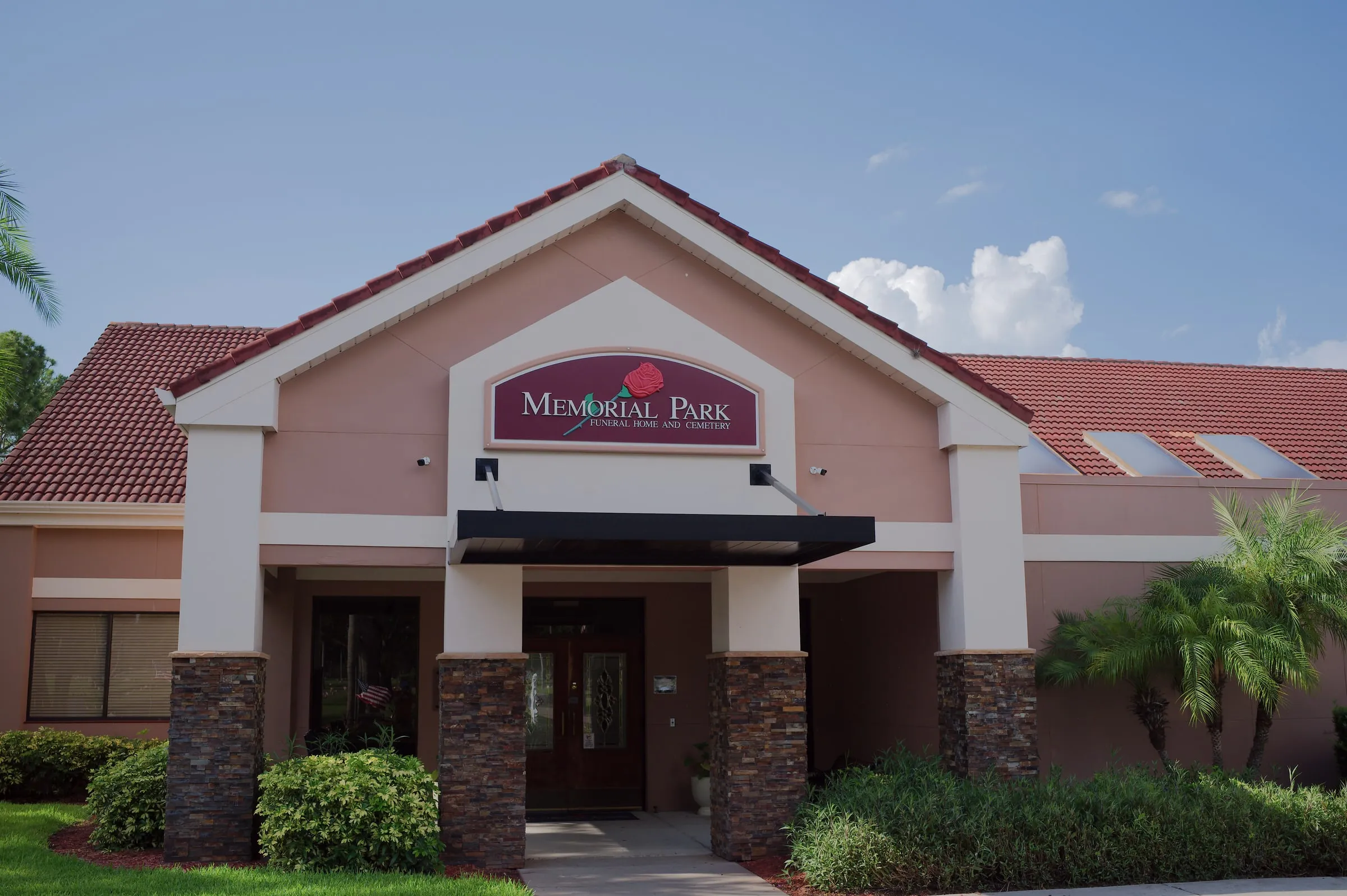 Funeral home entrance with a red tiled roof, arched sign and landscaping under a blue sky