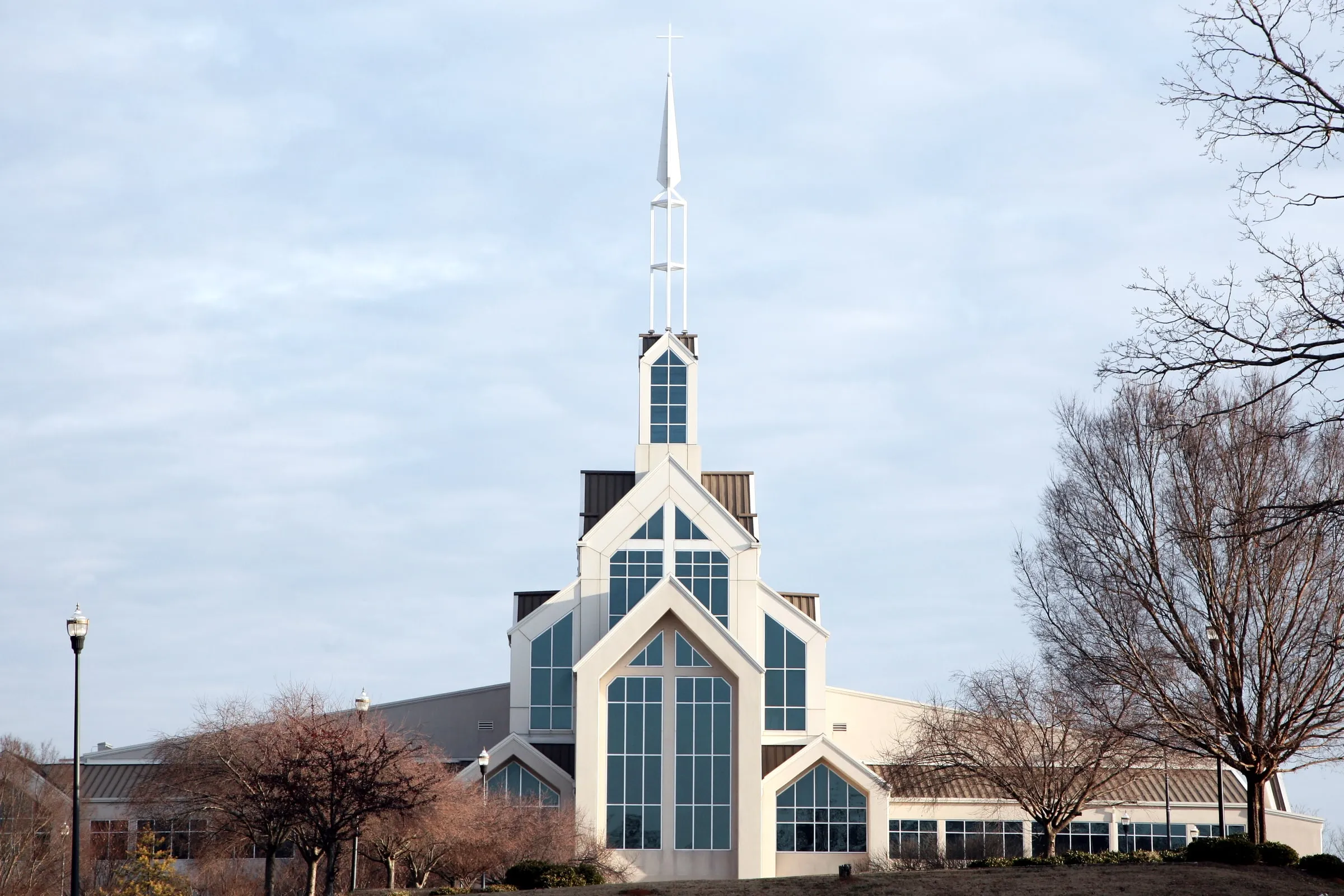 Modern church with a tall glass facade and steeple beside bare winter trees