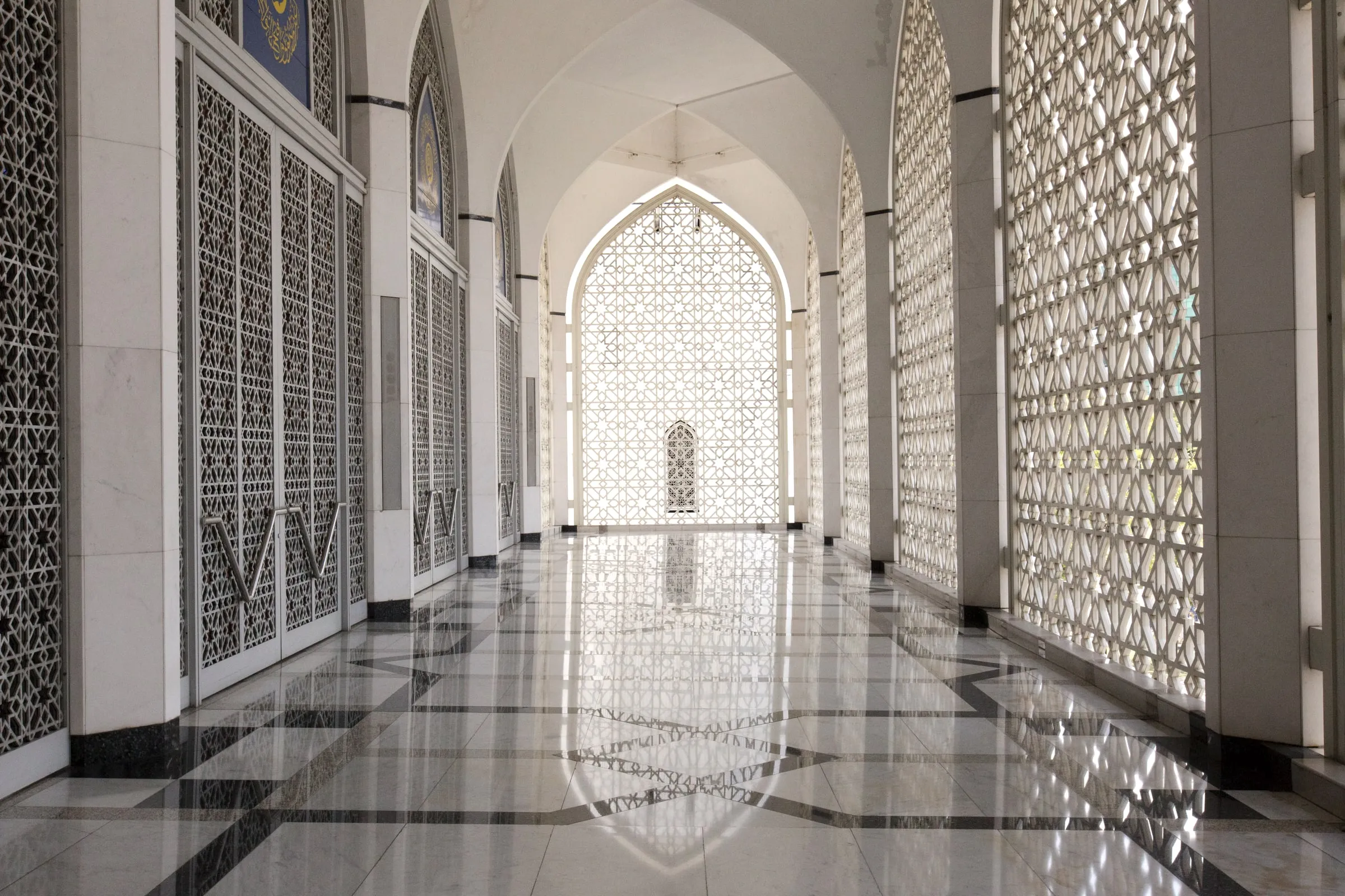 Mosque interior with pointed arches, carved screens and a polished floor reflecting the light