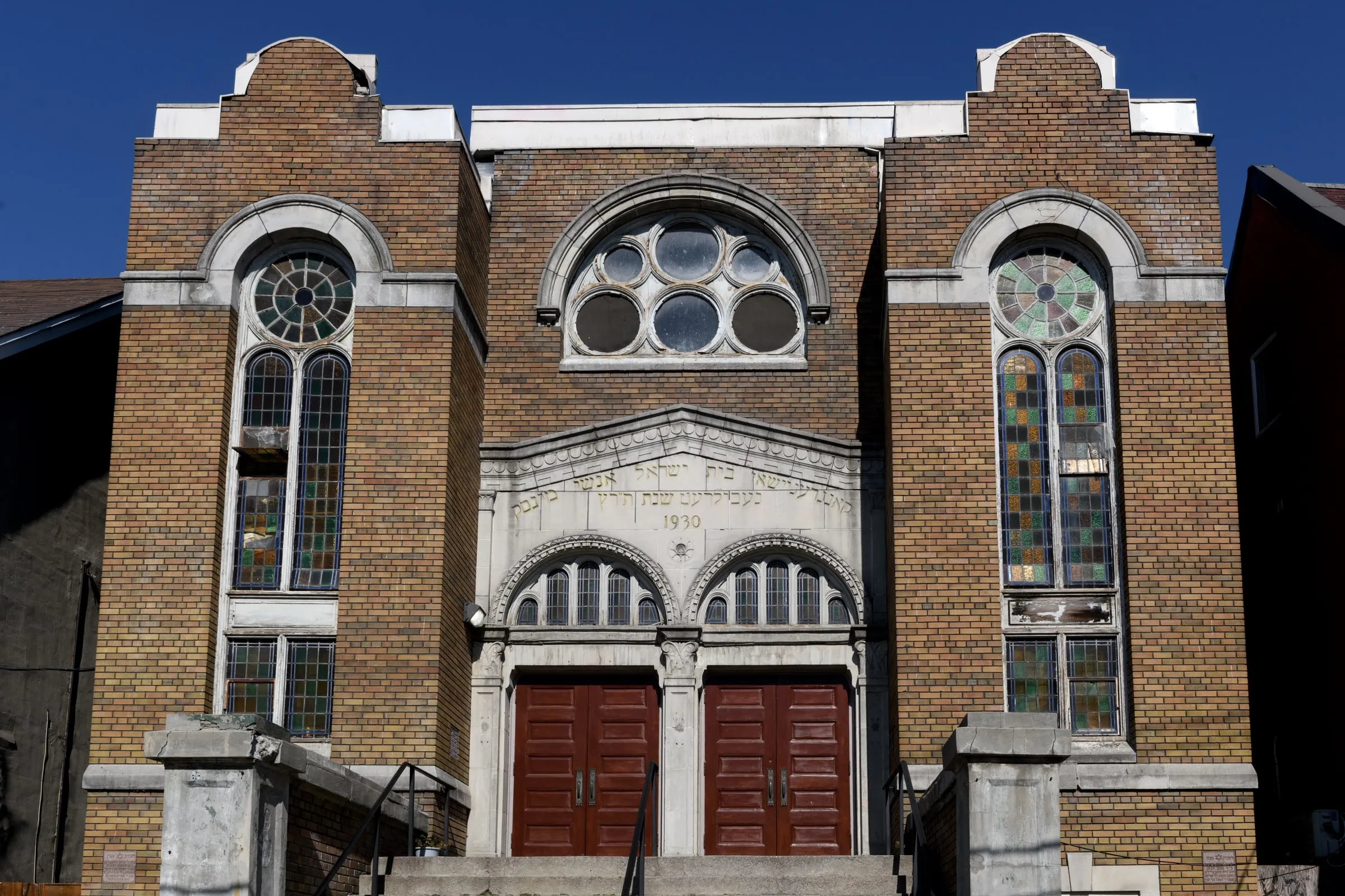 Brick synagogue facade with round windows, arched entry and dark double doors