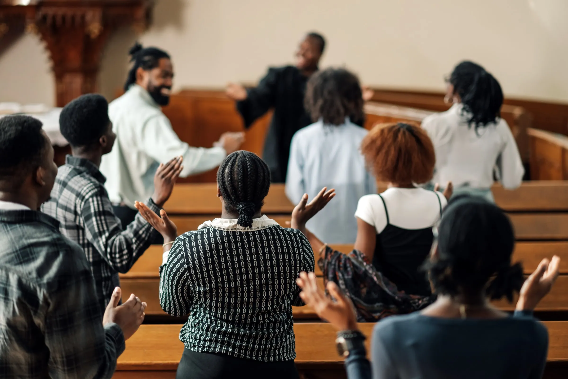 Congregation standing in wooden pews with raised hands during a worship service