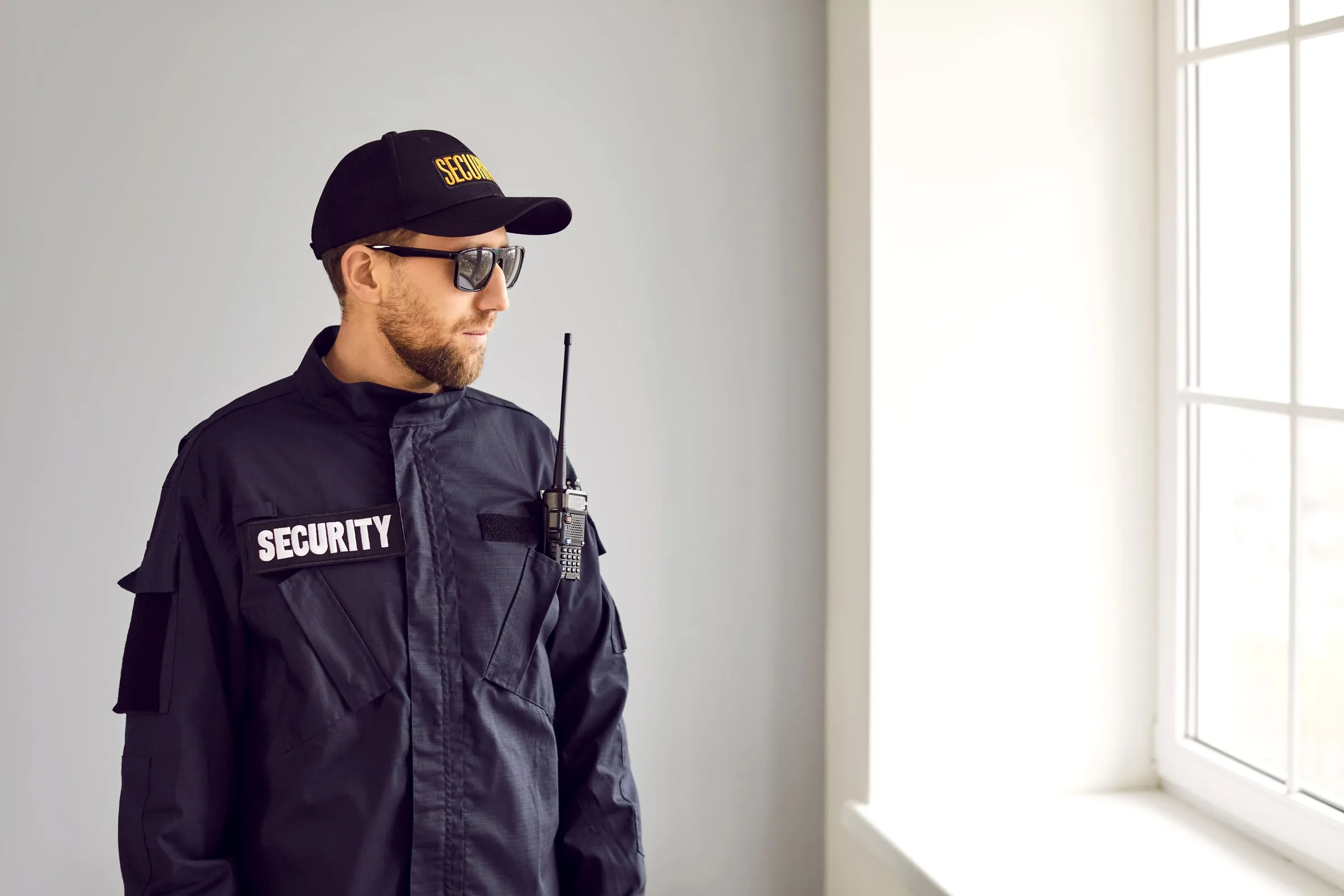 Security officer in a dark SECURITY jacket with a radio on the shoulder, looking out through a window