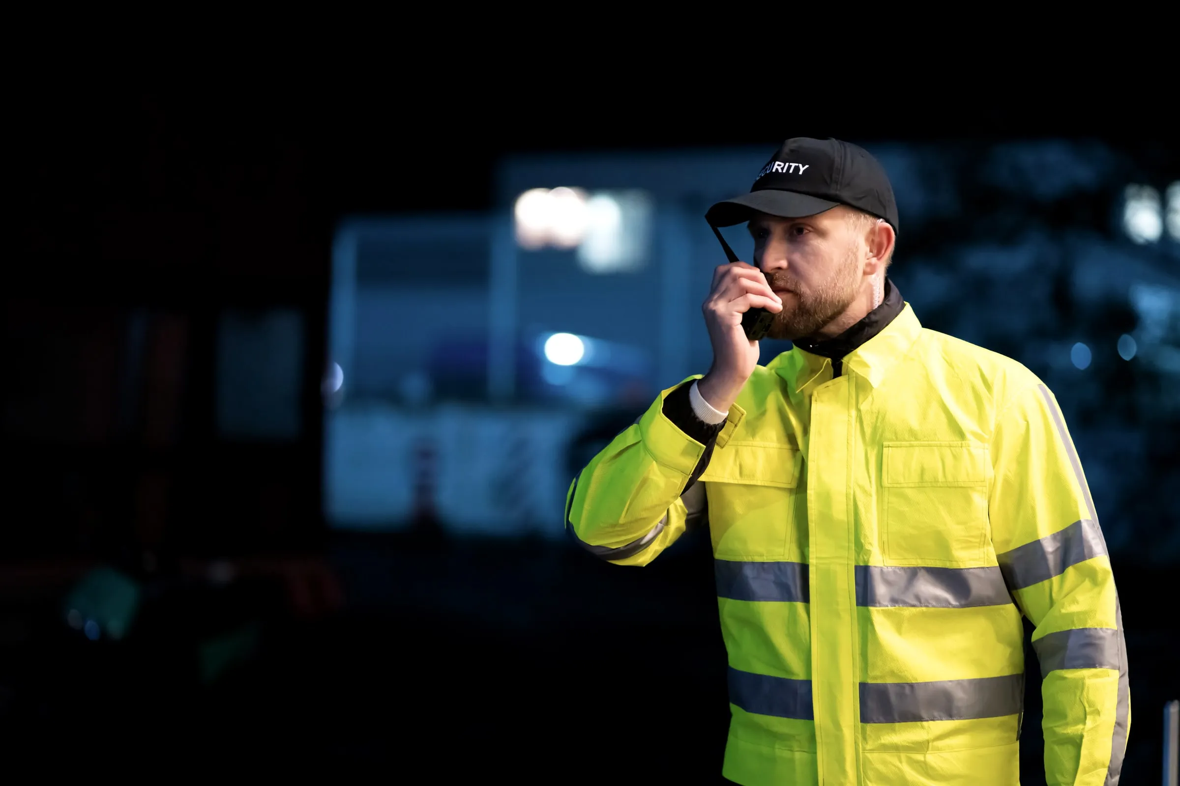 Close-up of a hand clipping a two-way radio microphone to the shoulder of a black uniform jacket at night